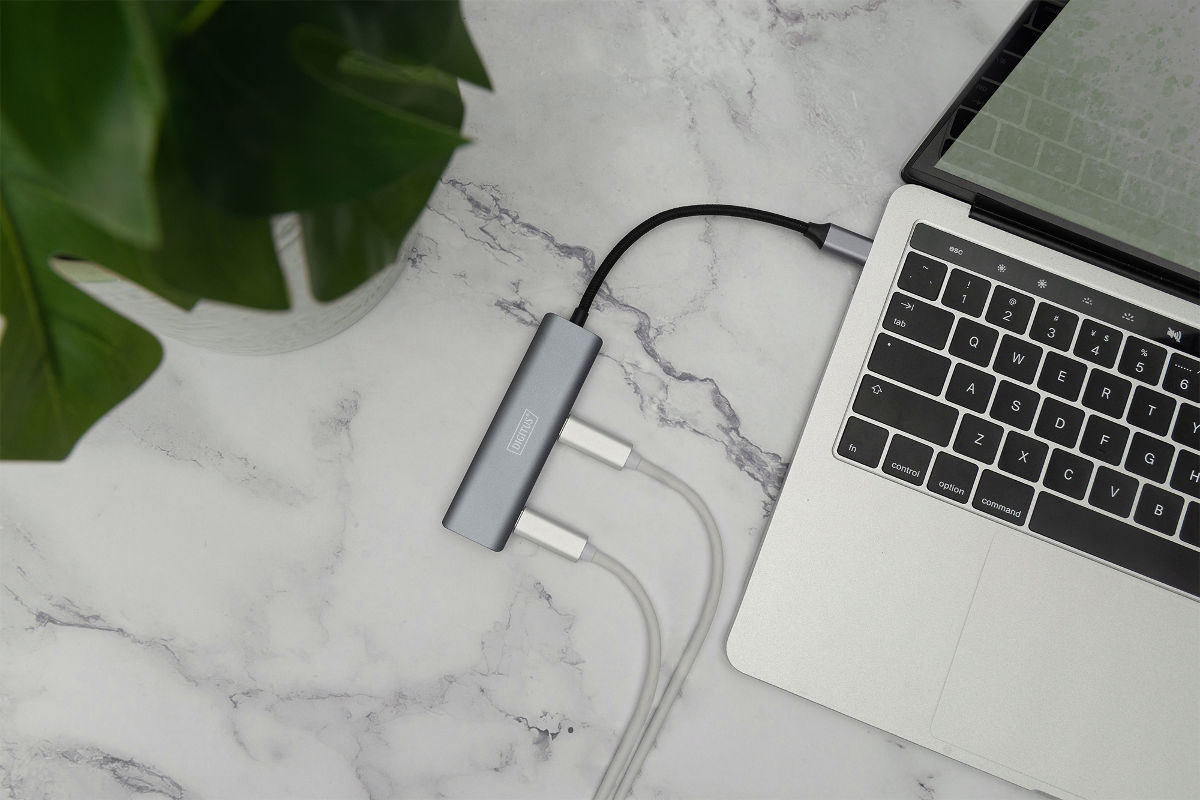 Grauer USB-C-Hub mit Kabeln, verbunden mit einem Laptop auf Marmortisch.