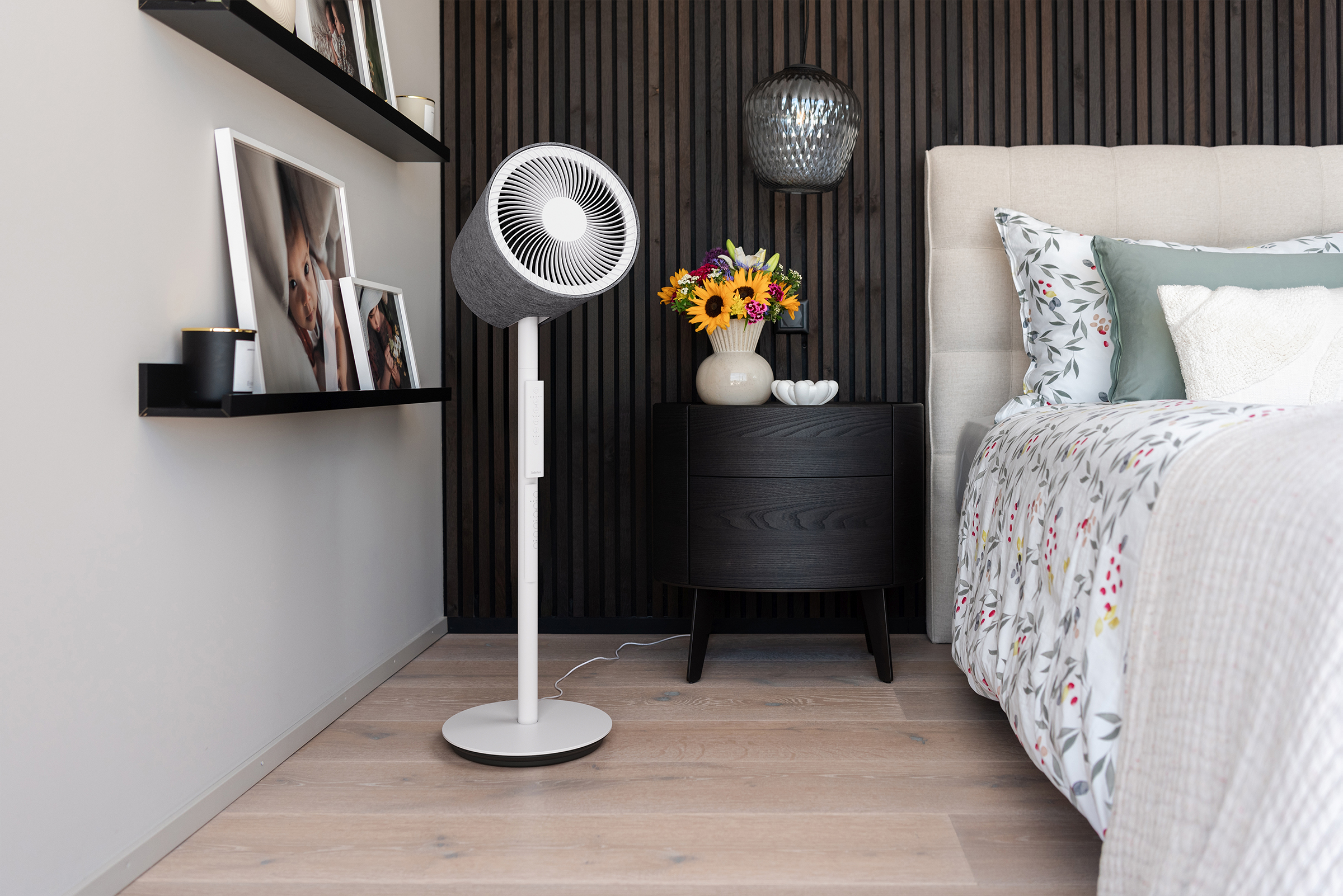 Ein Schlafzimmer mit einem Bett, Nachttisch, Ventilator und Fotos an der Wand.