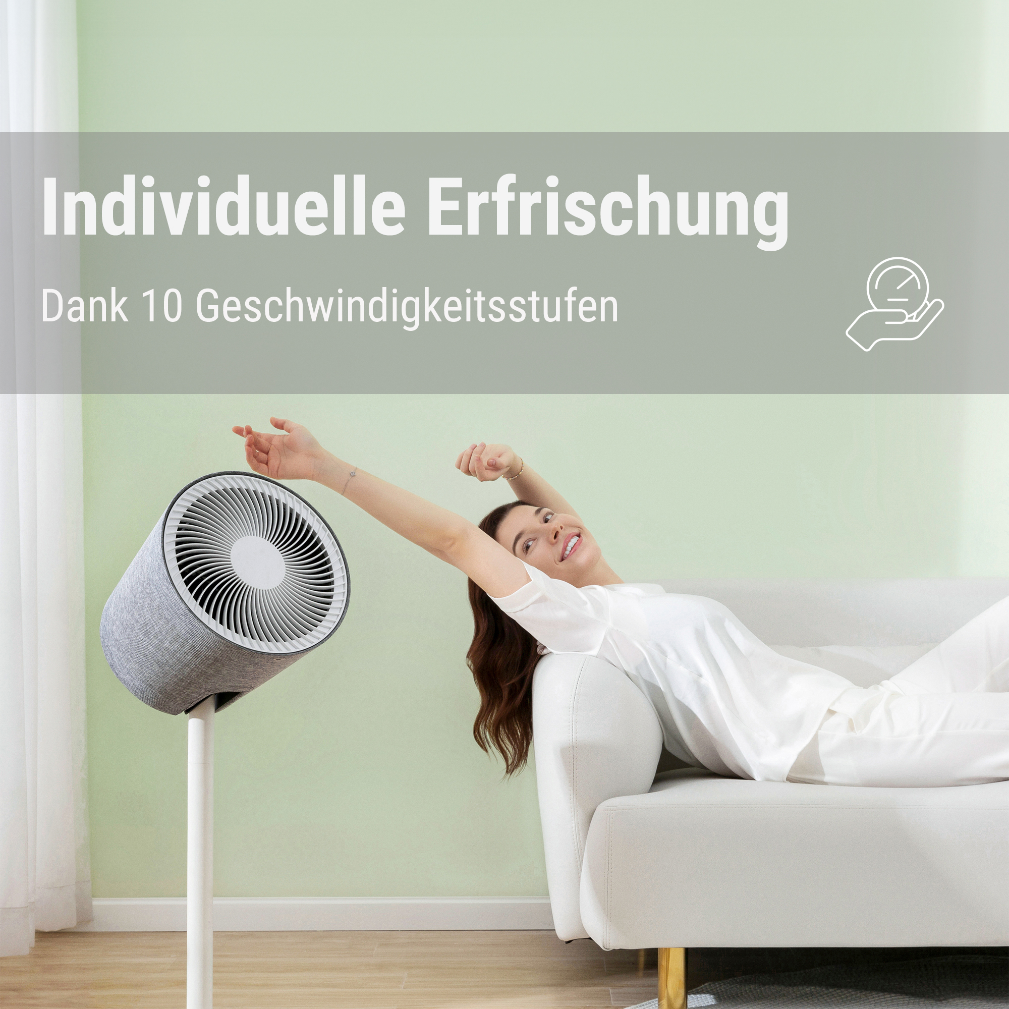 Eine Frau streckt sich auf einem weißen Sofa neben einem modernen grauen Ventilator auf einem Ständer vor einer hellgrünen Wand.