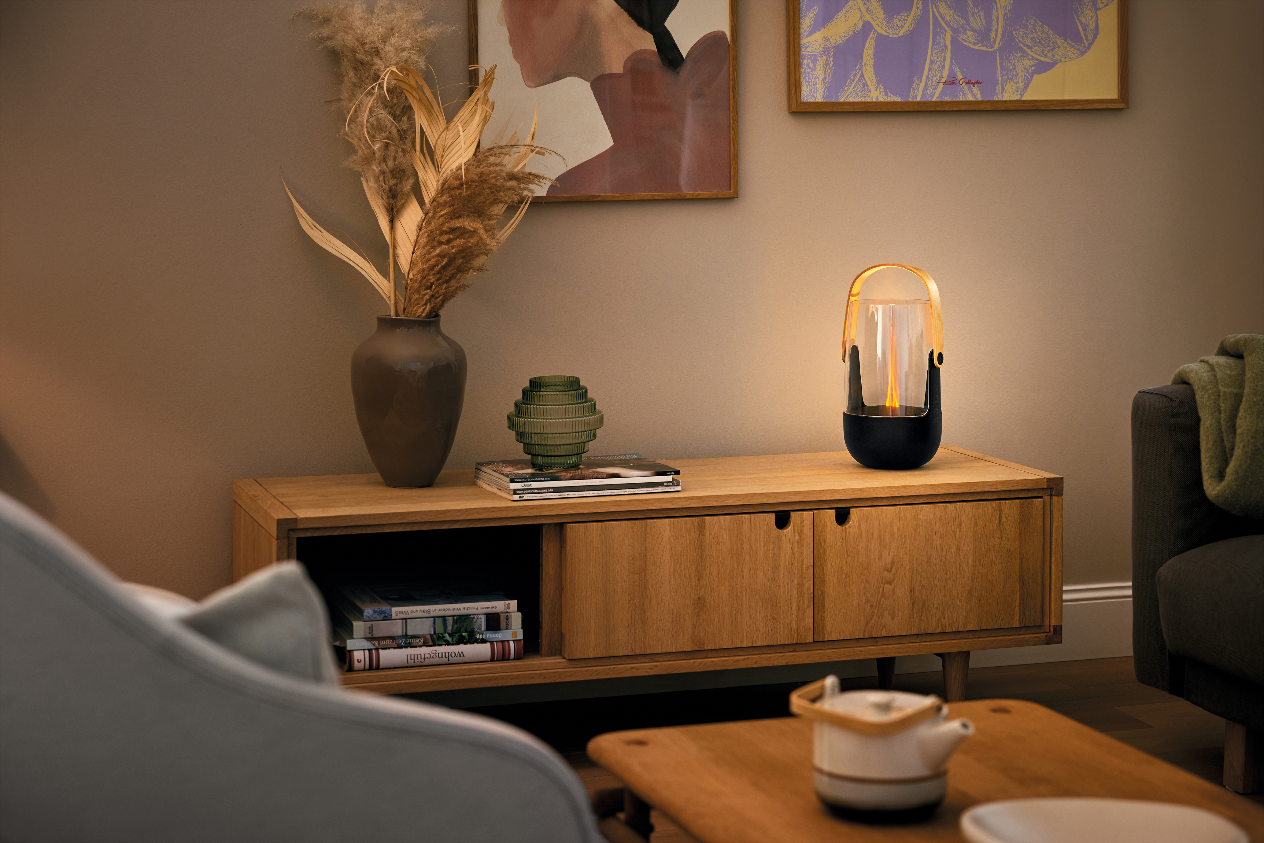 Ein Nachttisch aus Holz mit Vase, Lampe, Bildern und Büchern.