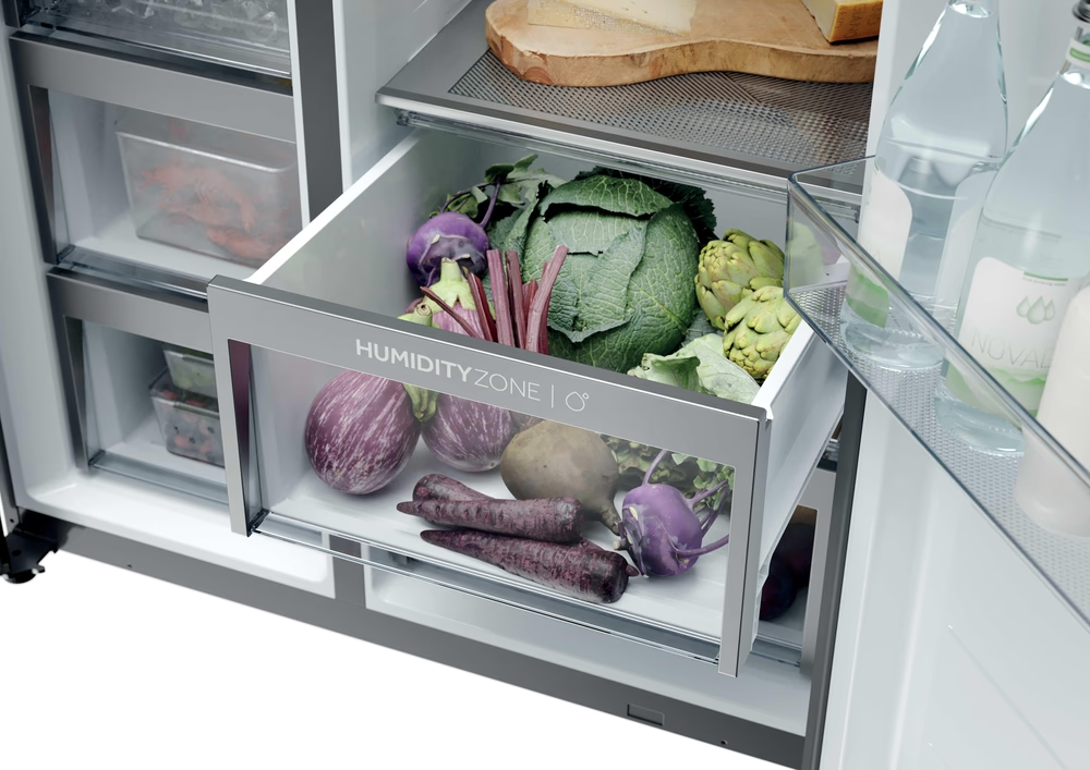 Ein offener Kühlschrank mit einer Schublade voller Gemüse wie Kohl, Auberginen und Karotten.