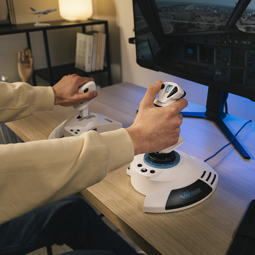 Manos operan joysticks frente a una pantalla de simulador de vuelo.