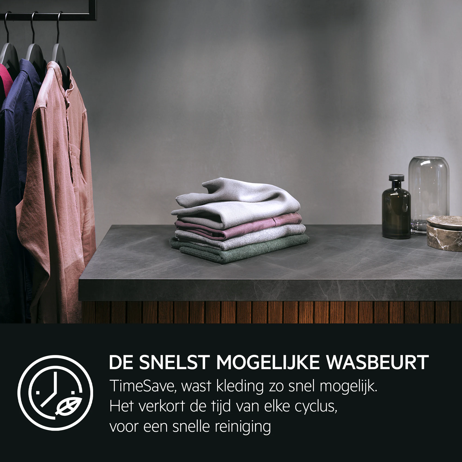 Kleding hangt aan hangers, een stapel gevouwen kleding rust op een aanrecht.