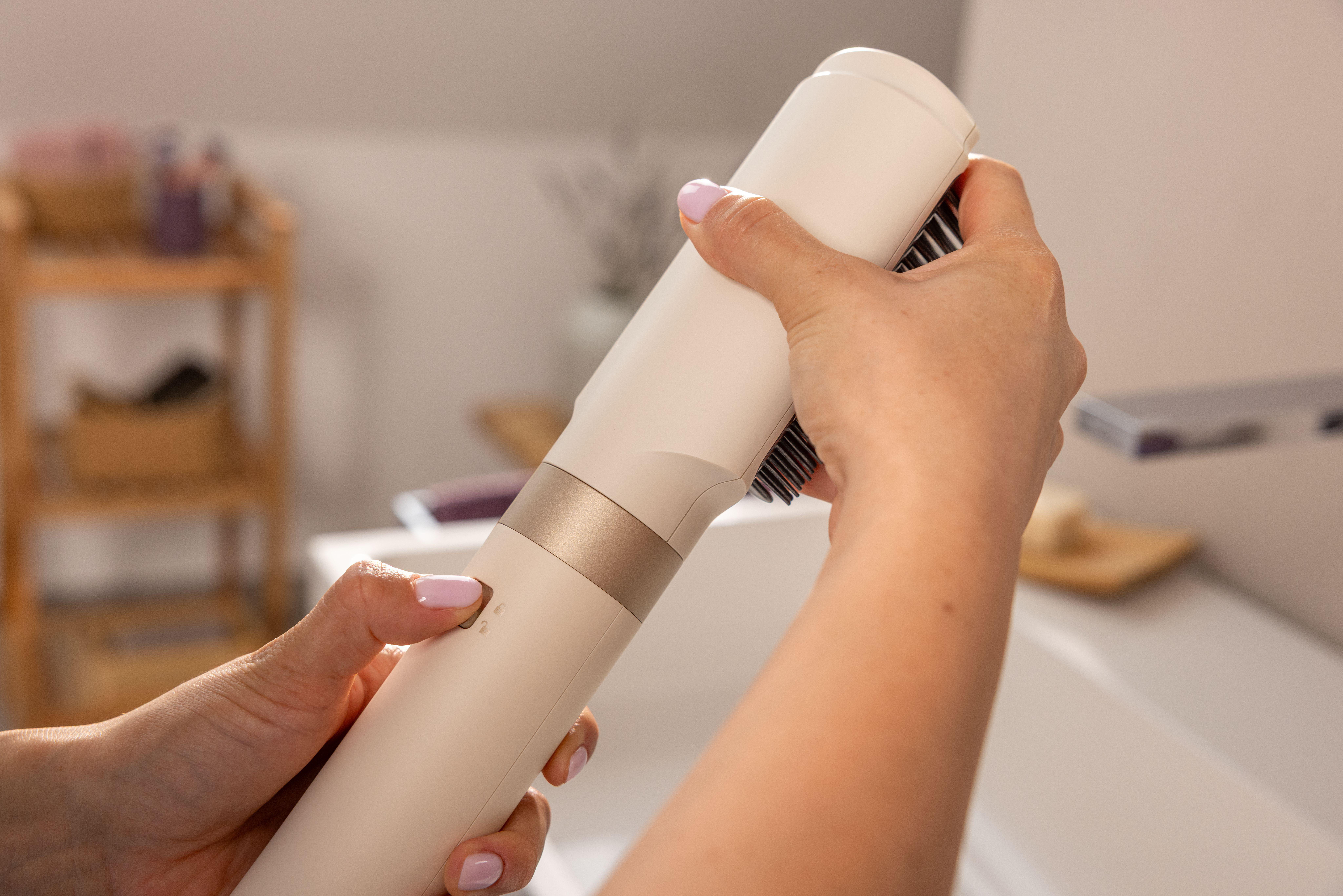 Eine Hand hält ein weißes Haarstyling-Gerät mit goldener Akzentuierung.