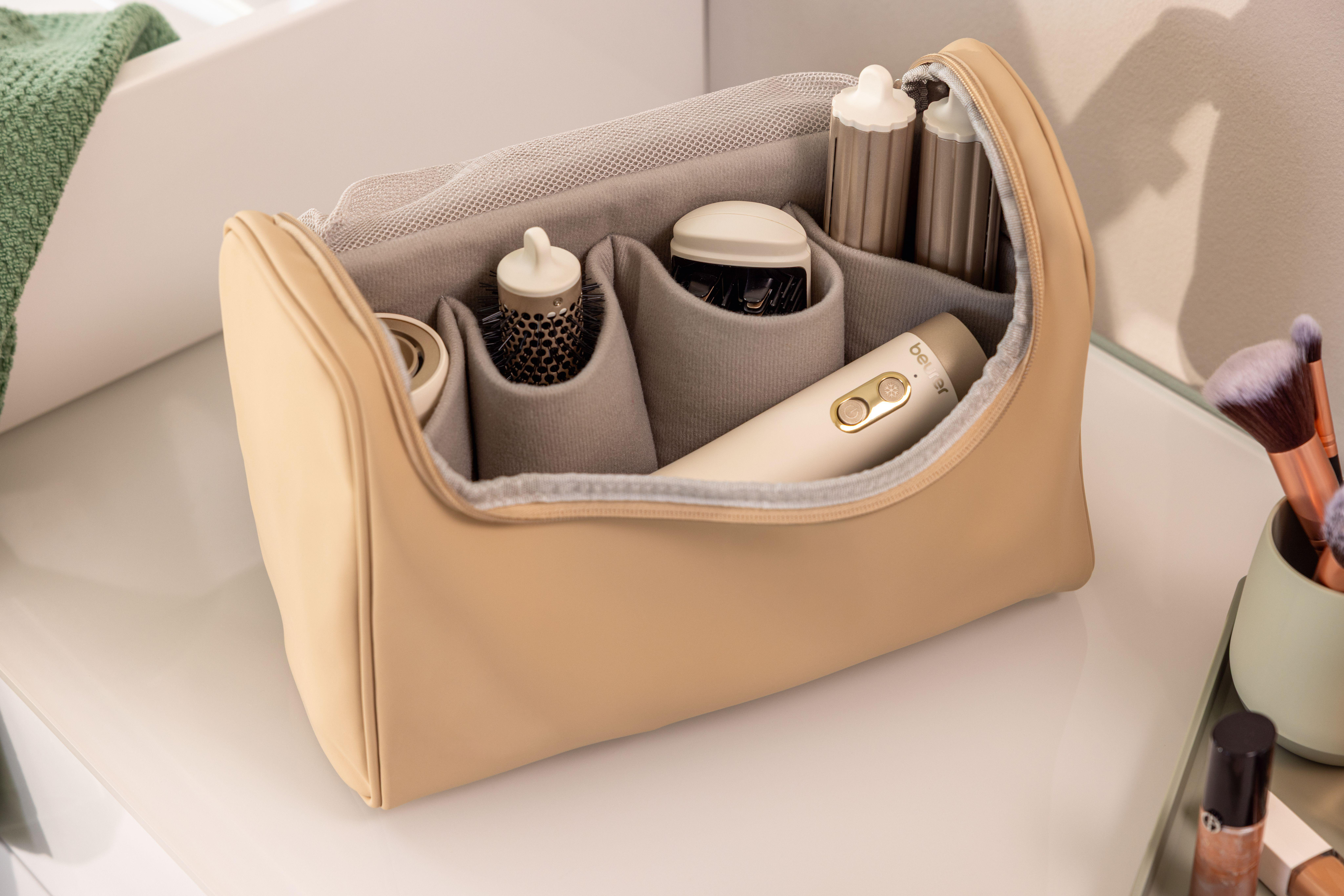 Beige Kosmetiktasche mit Haartrockner, Bürsten und Lockenwicklern.