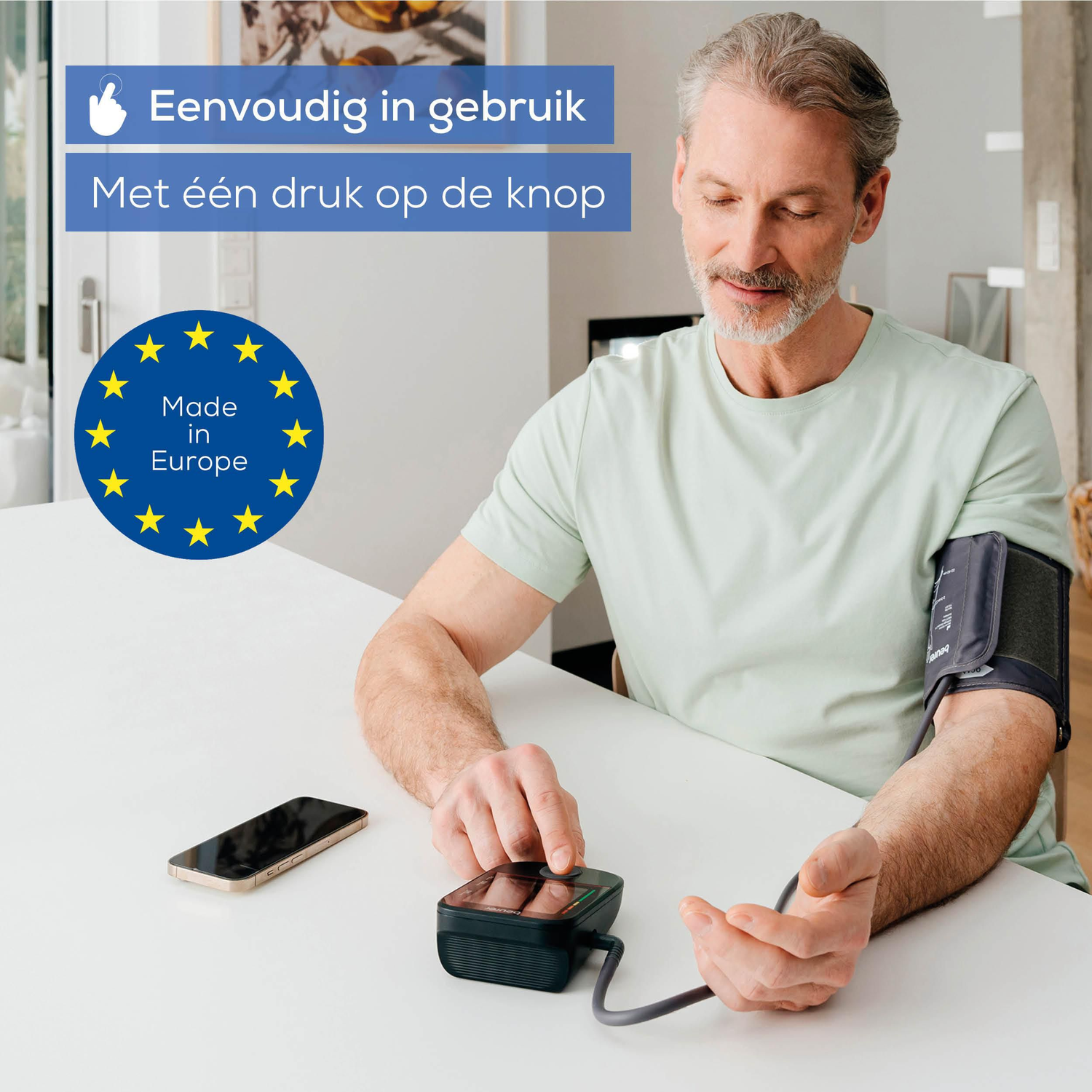 Man measures blood pressure with device, phone, and EU stars circle on table.