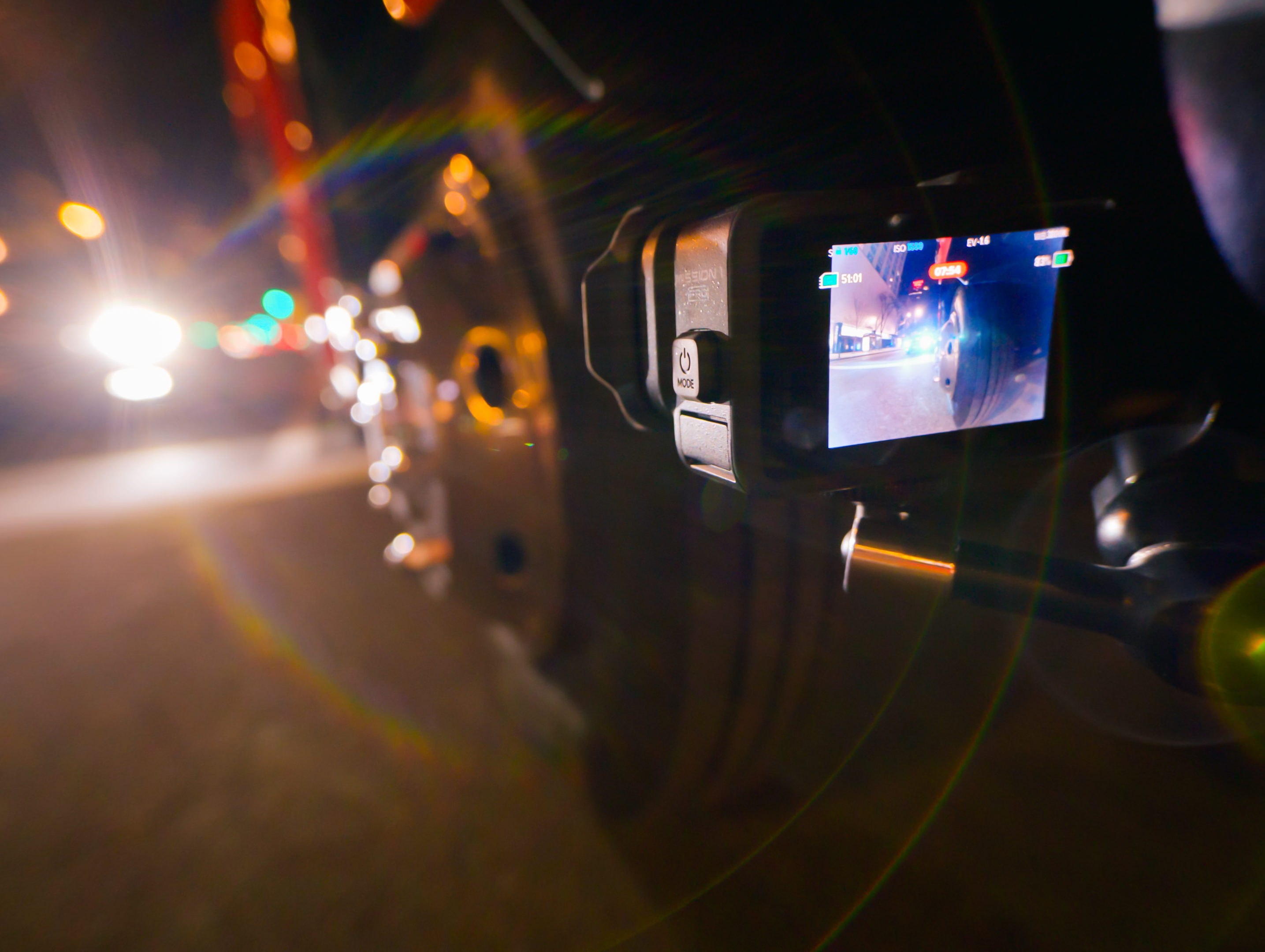Kamera sportowa zamontowana na pojeździe w nocy, pokazująca światła miasta i ruch. Efekt bokeh.