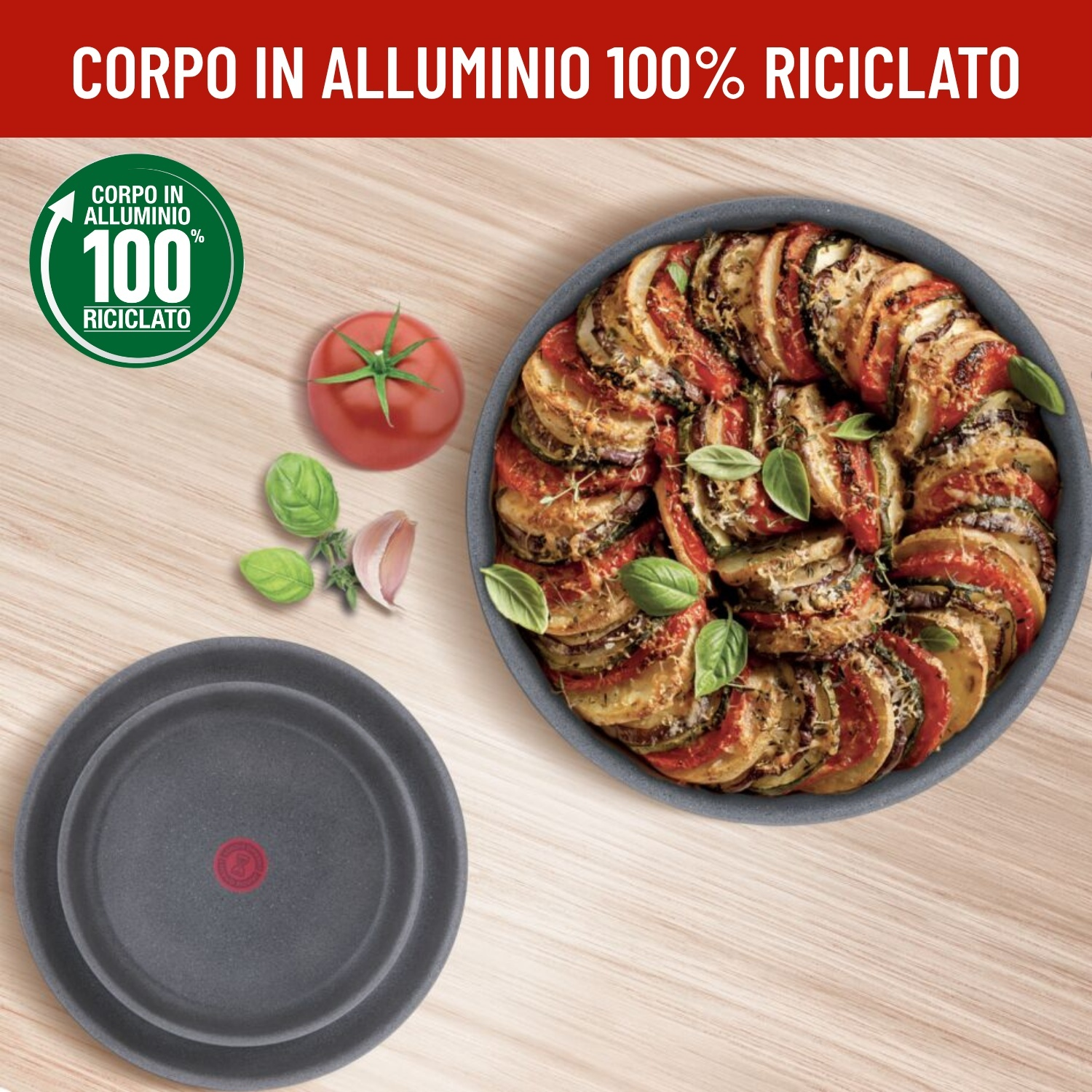 Gratin di pomodoro e zucchine in padella, con pomodoro e aglio accanto.