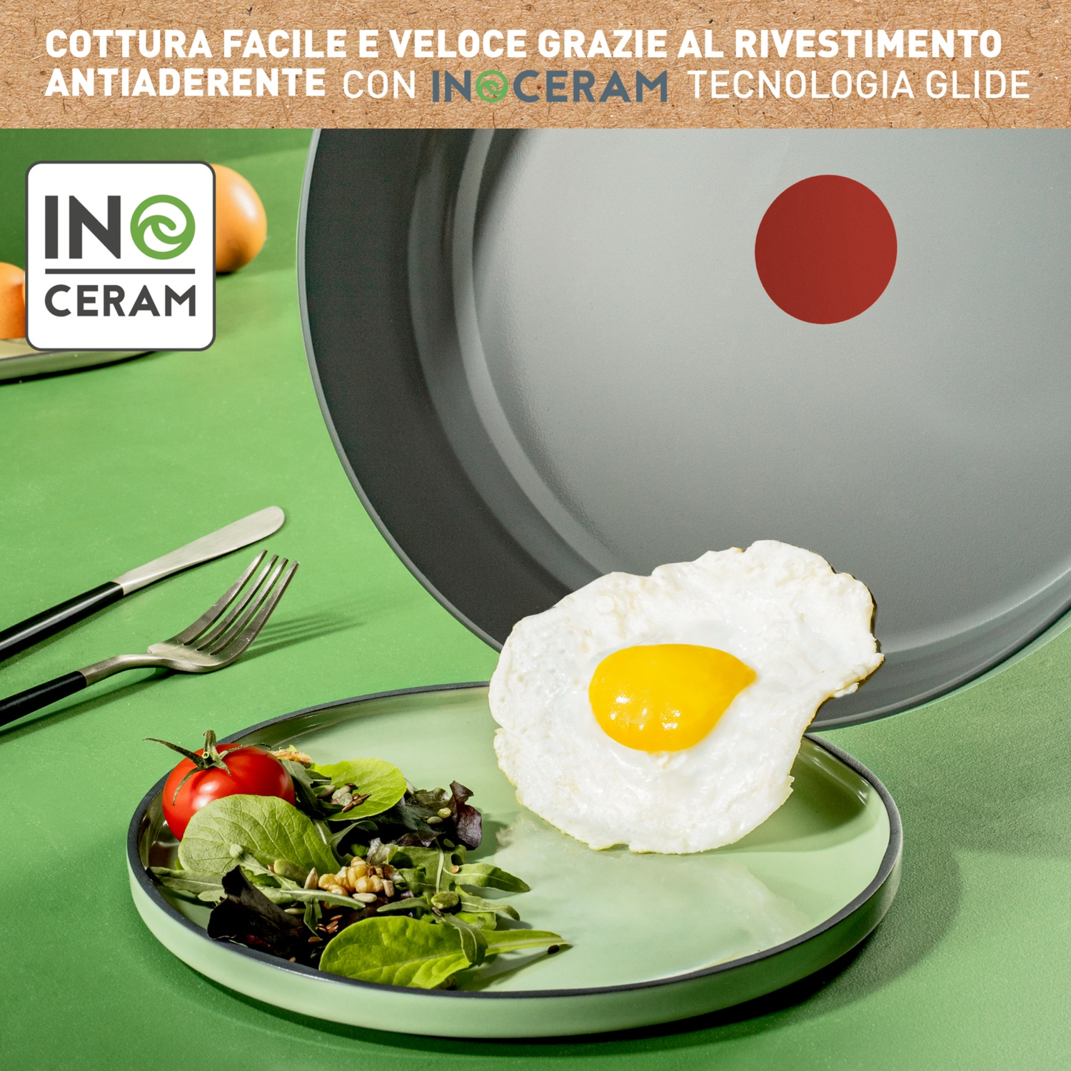 Un uovo fritto su un piatto con insalata e posate, padella sullo sfondo.