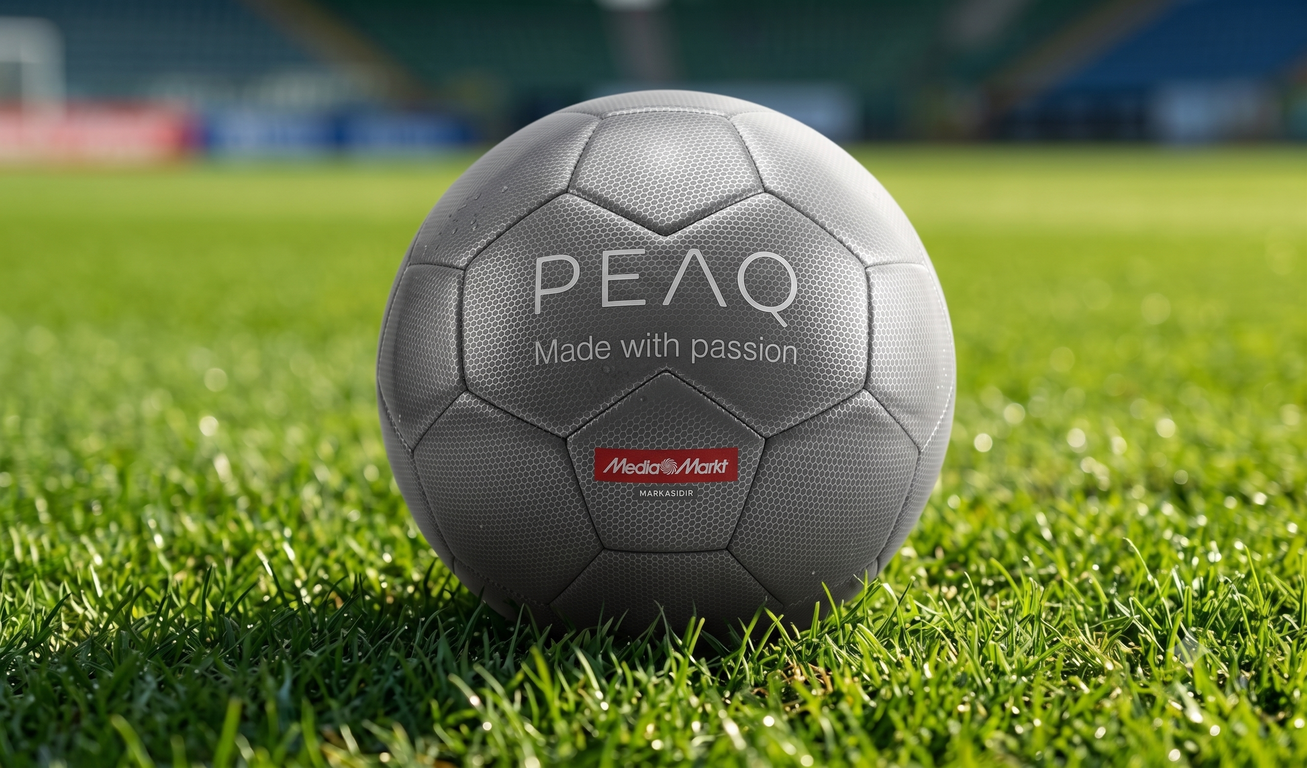 Yeşil futbol sahasında "PEAQ Made with passion" logolu gri futbol topu.