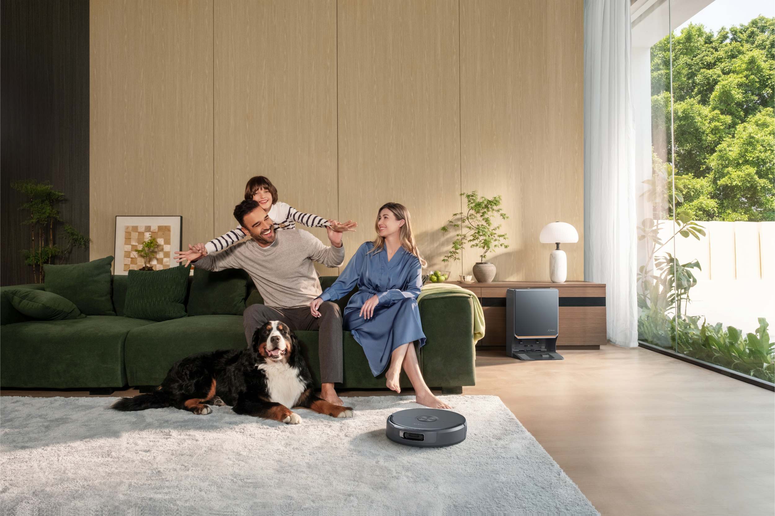 Familie auf Sofa mit Hund, Roboterstaubsauger und Aussicht auf Garten.