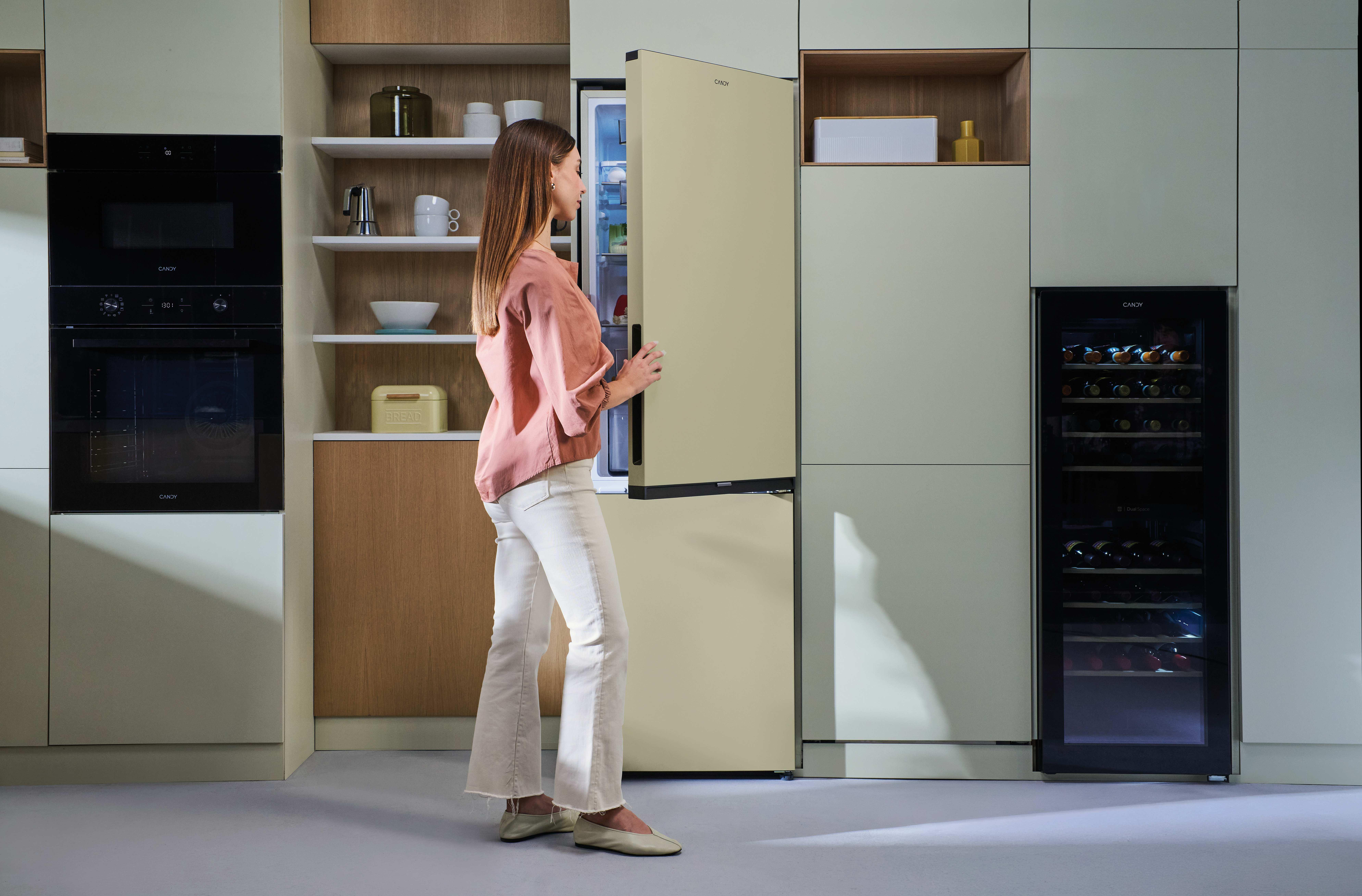 Eine Frau öffnet einen cremefarbenen Kühlschrank in einer modernen Küche mit Öfen.