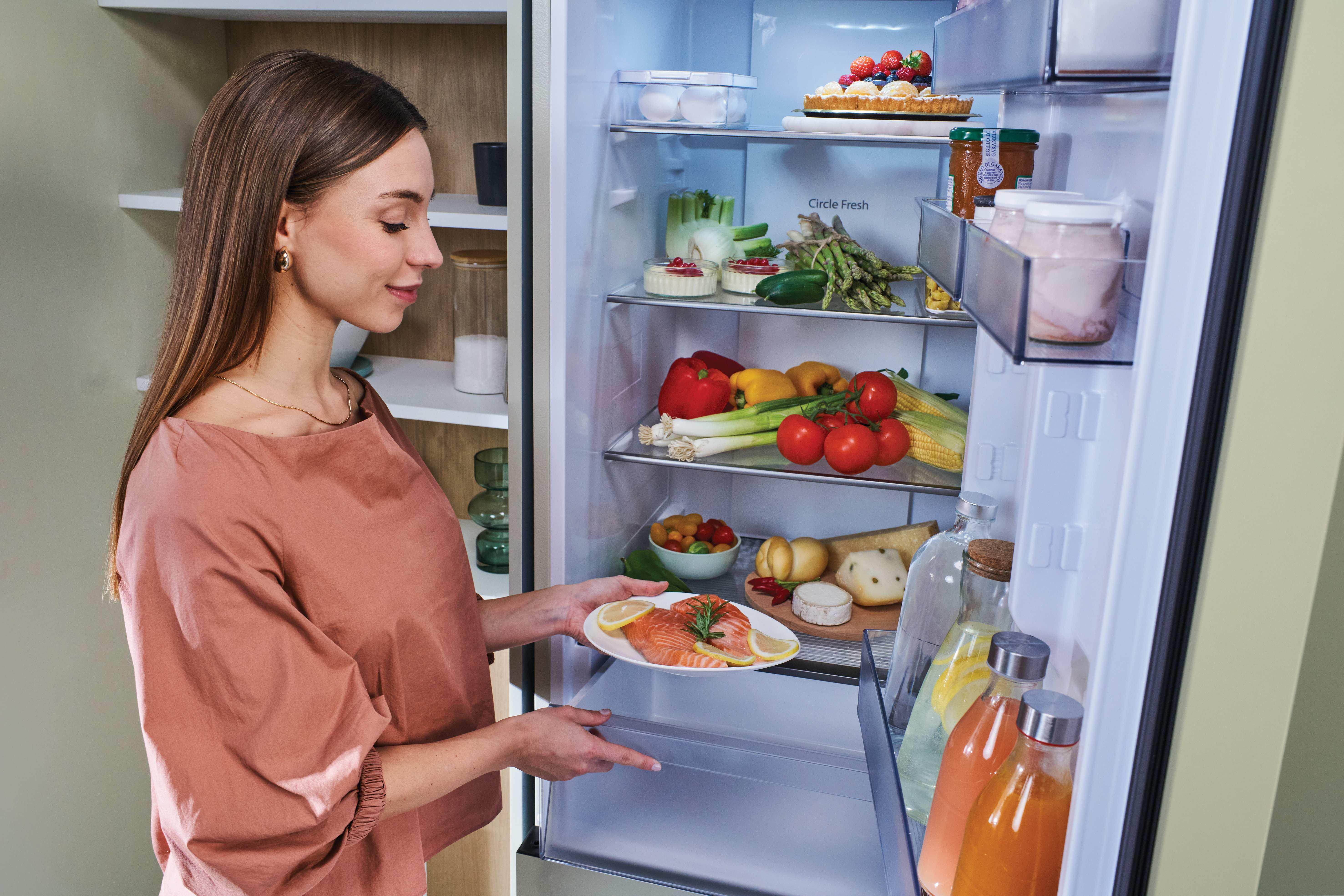 Eine Frau legt Lachs mit Zitrone in einen gut gefüllten Kühlschrank.
