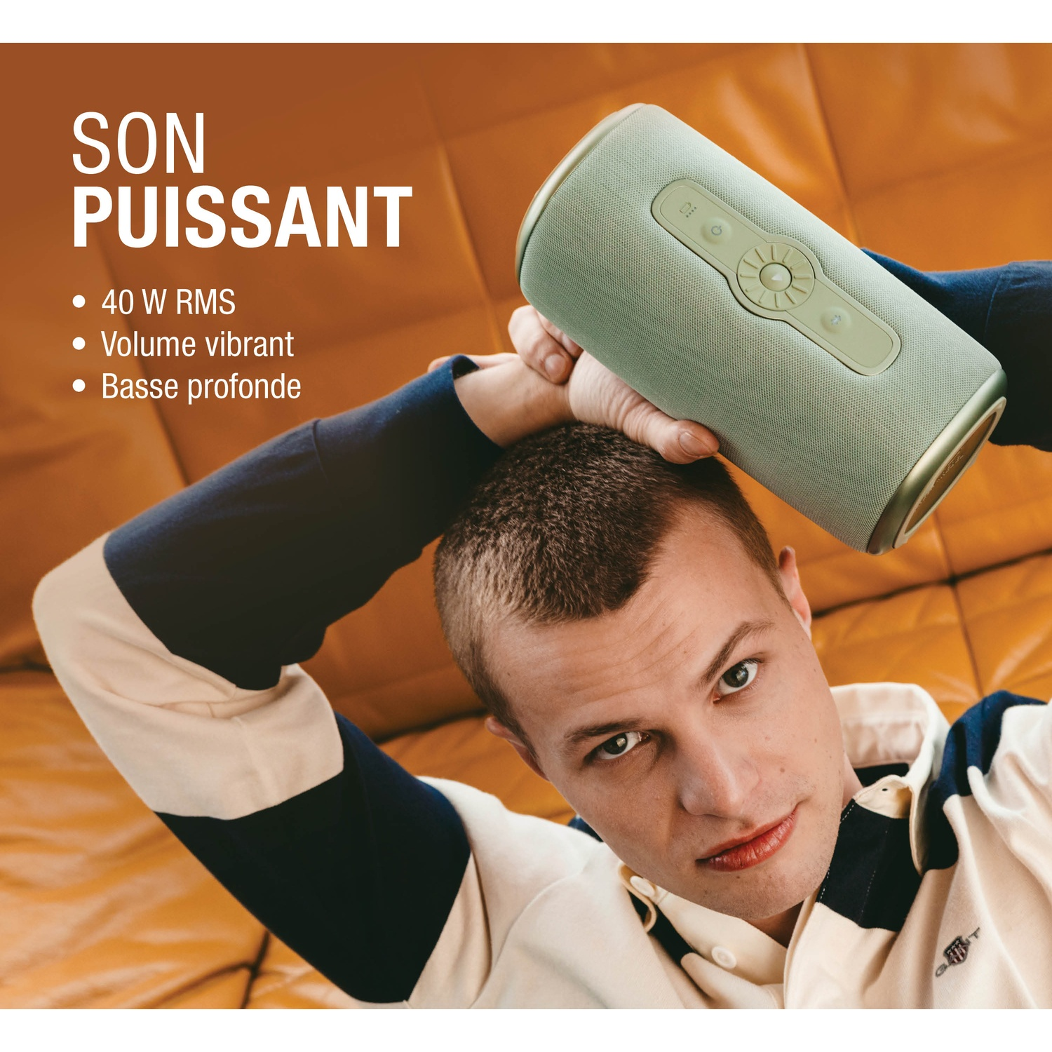 Un homme avec une enceinte vert clair au-dessus de sa tête sur un canapé marron.