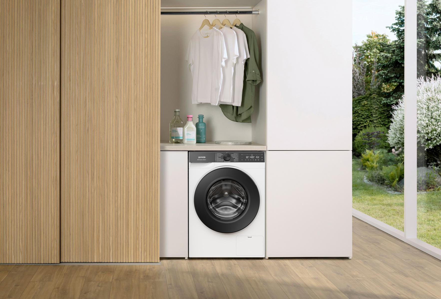 Eine Waschmaschine mit weißer Front und schwarzer Tür steht neben einem Holzschrank.