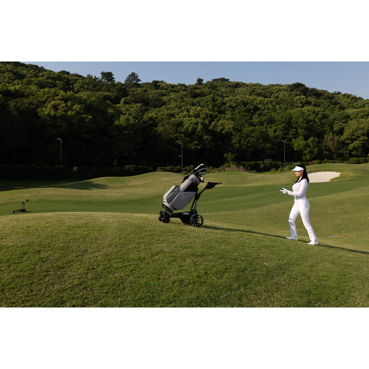 Une femme en blanc sur un terrain de golf avec un chariot et beaucoup de verdure.