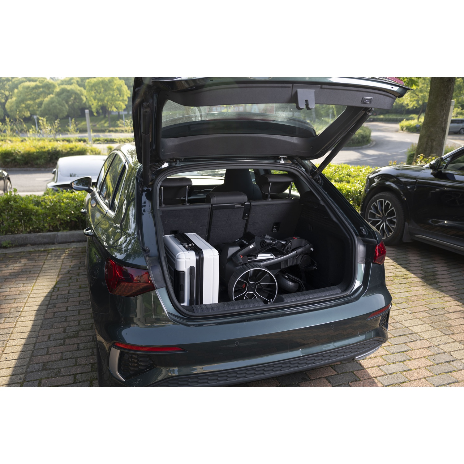 Un break foncé, coffre ouvert, avec une poussette et une valise à l'intérieur.