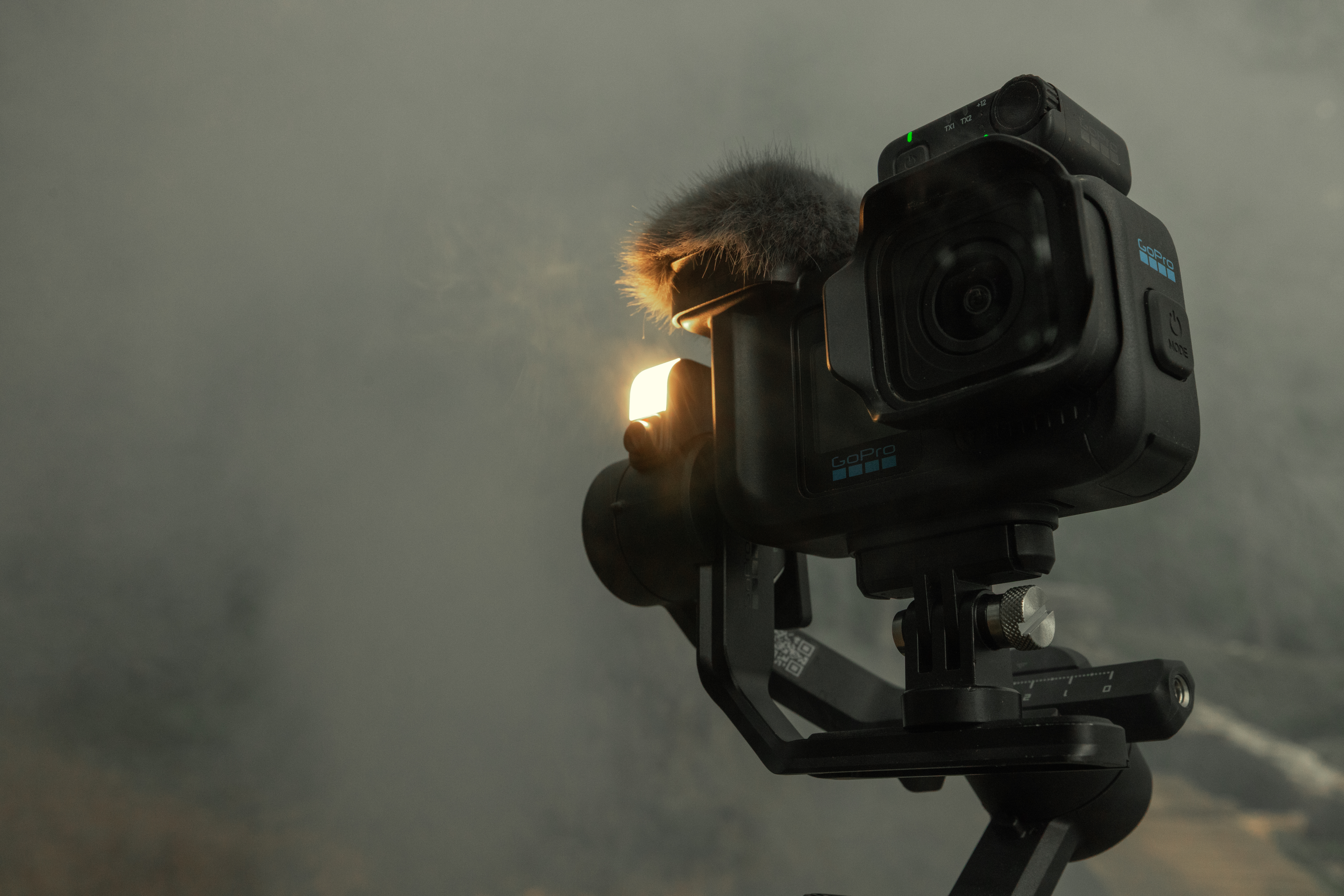 Czarna kamera GoPro z mikrofonem i światłem na gimbalu na mglistym tle.