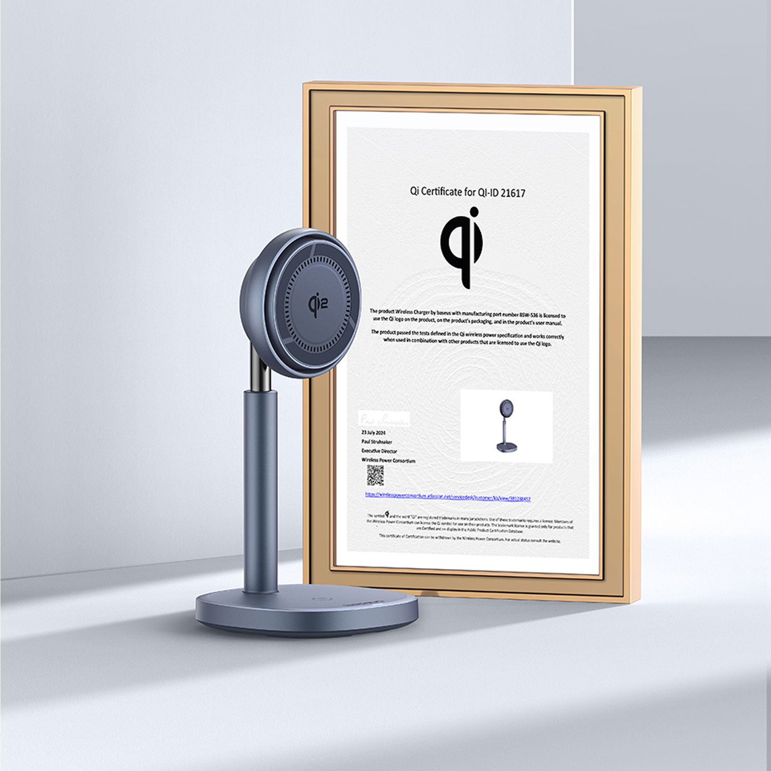 Un cargador Qi gris junto a un certificado Qi en un marco dorado.