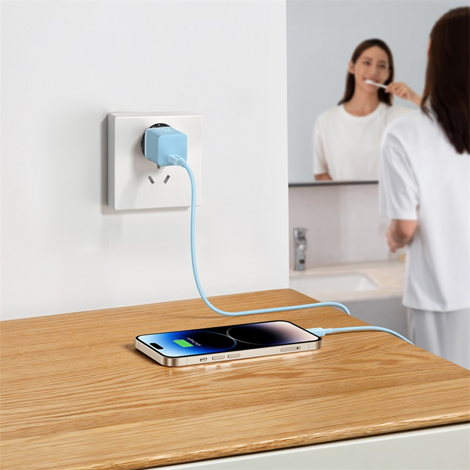 Un cargador azul enchufado a un enchufe de pared, cargando un teléfono en una mesa de madera.