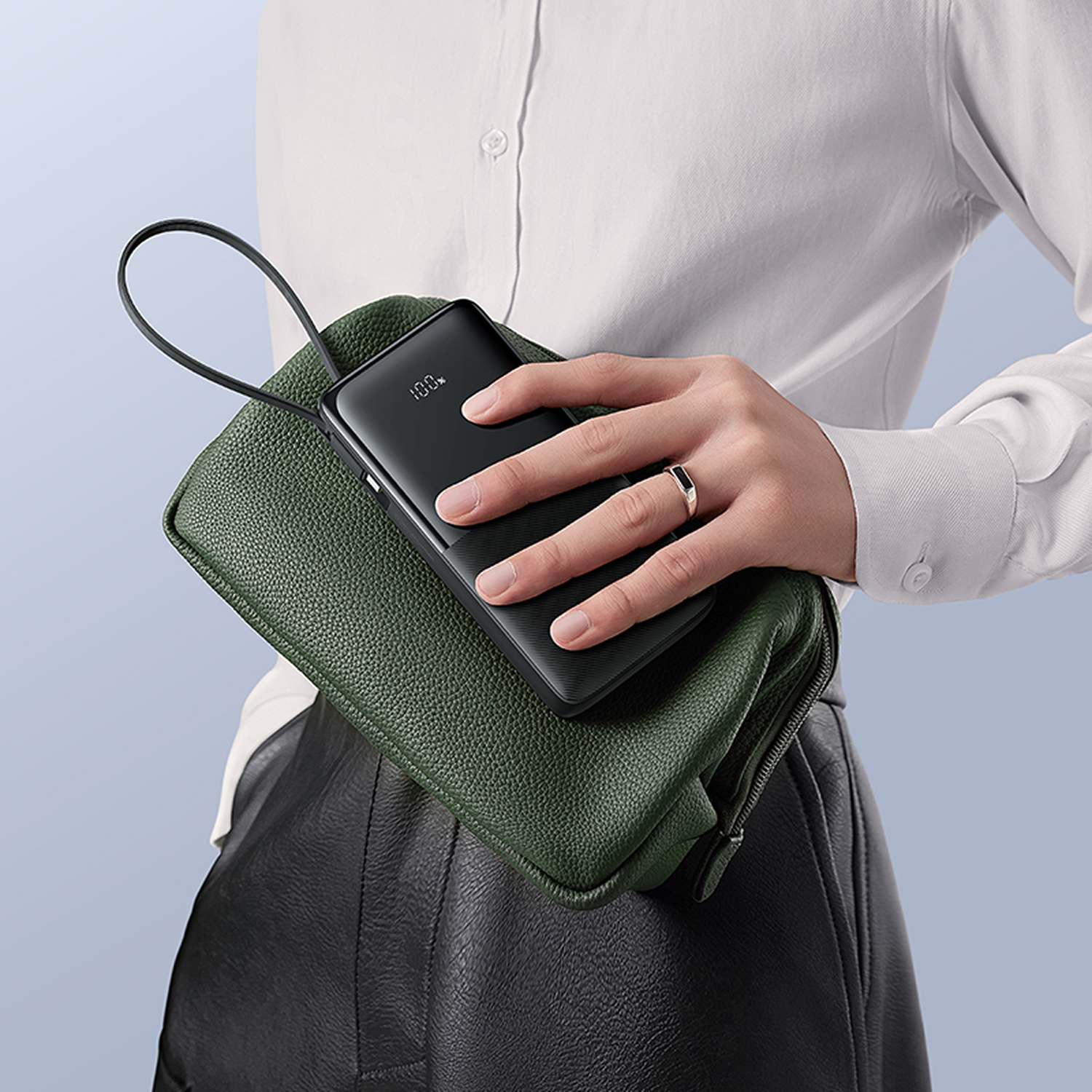 Una mano sostiene un cargador negro con 100% de carga sobre un bolso verde.