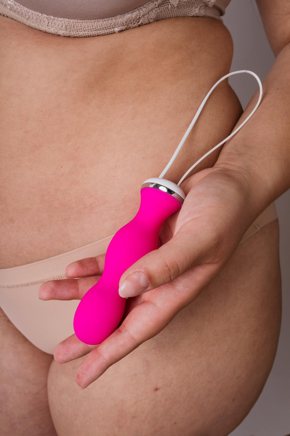 Eine Hand hält einen leuchtend pinken Vibrator mit weißem Kabel.
