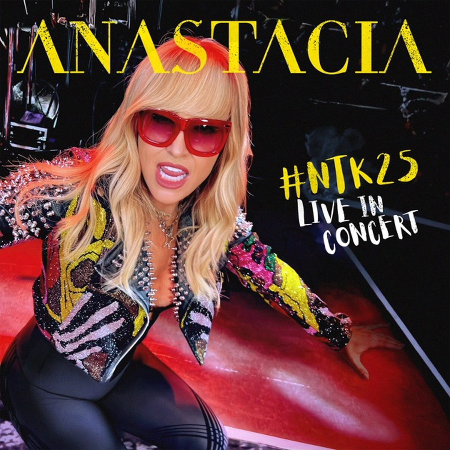 Anastacia met rode zonnebril en glitterjas zingt live op het podium.