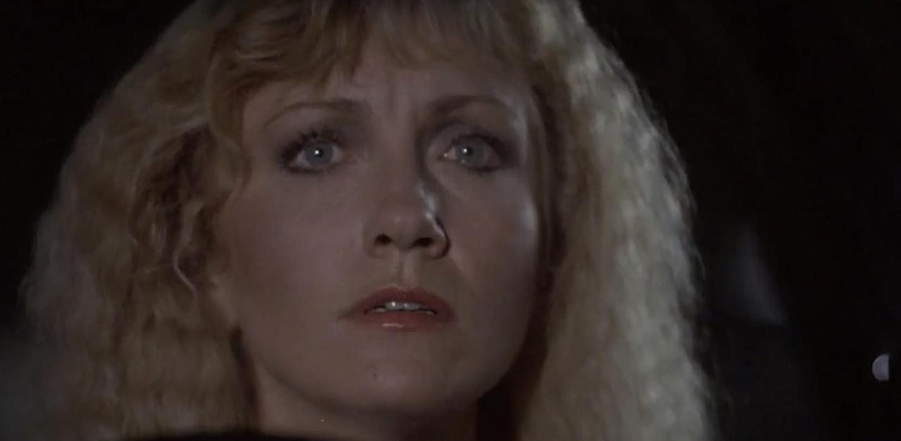 Eine Frau mit blonden Haaren blickt mit weit aufgerissenen Augen nach vorne.