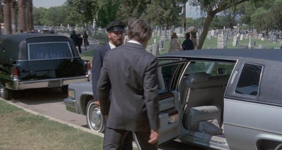 Ein Bestattungswagen und eine Limousine stehen auf einem Friedhof neben Grabsteinen.