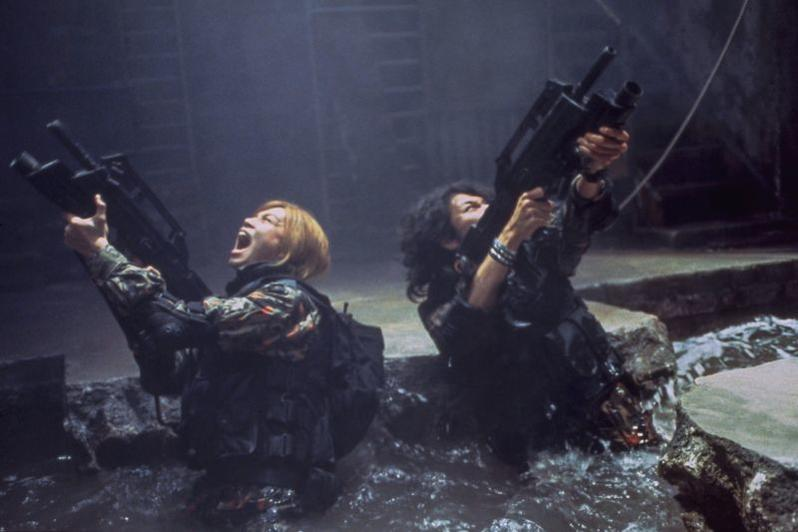 Zwei Frauen mit Waffen im Wasser, eine schreit, die andere zielt.