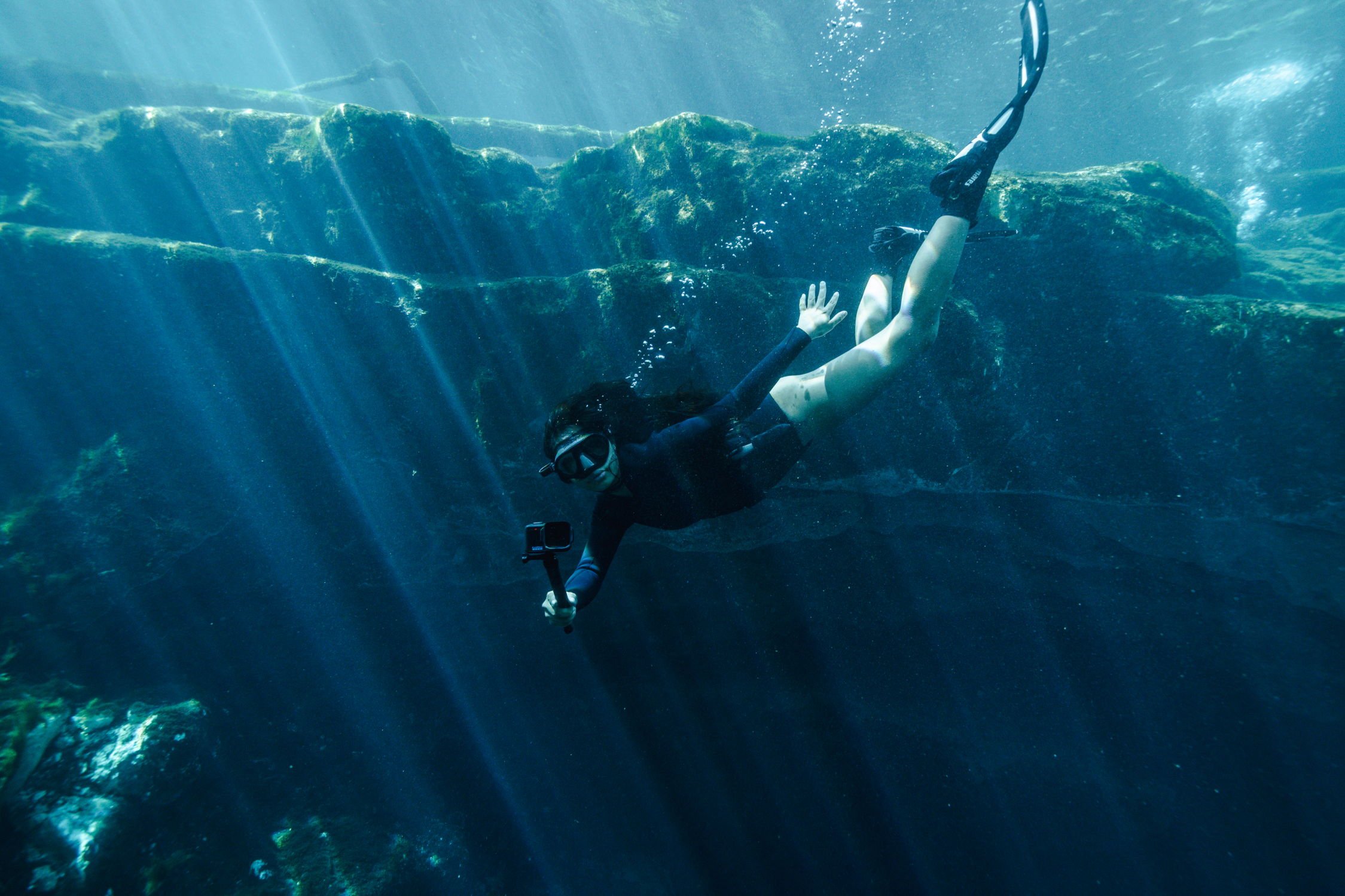 Eine Person schnorchelt unter Wasser mit einer Kamera und Flossen.