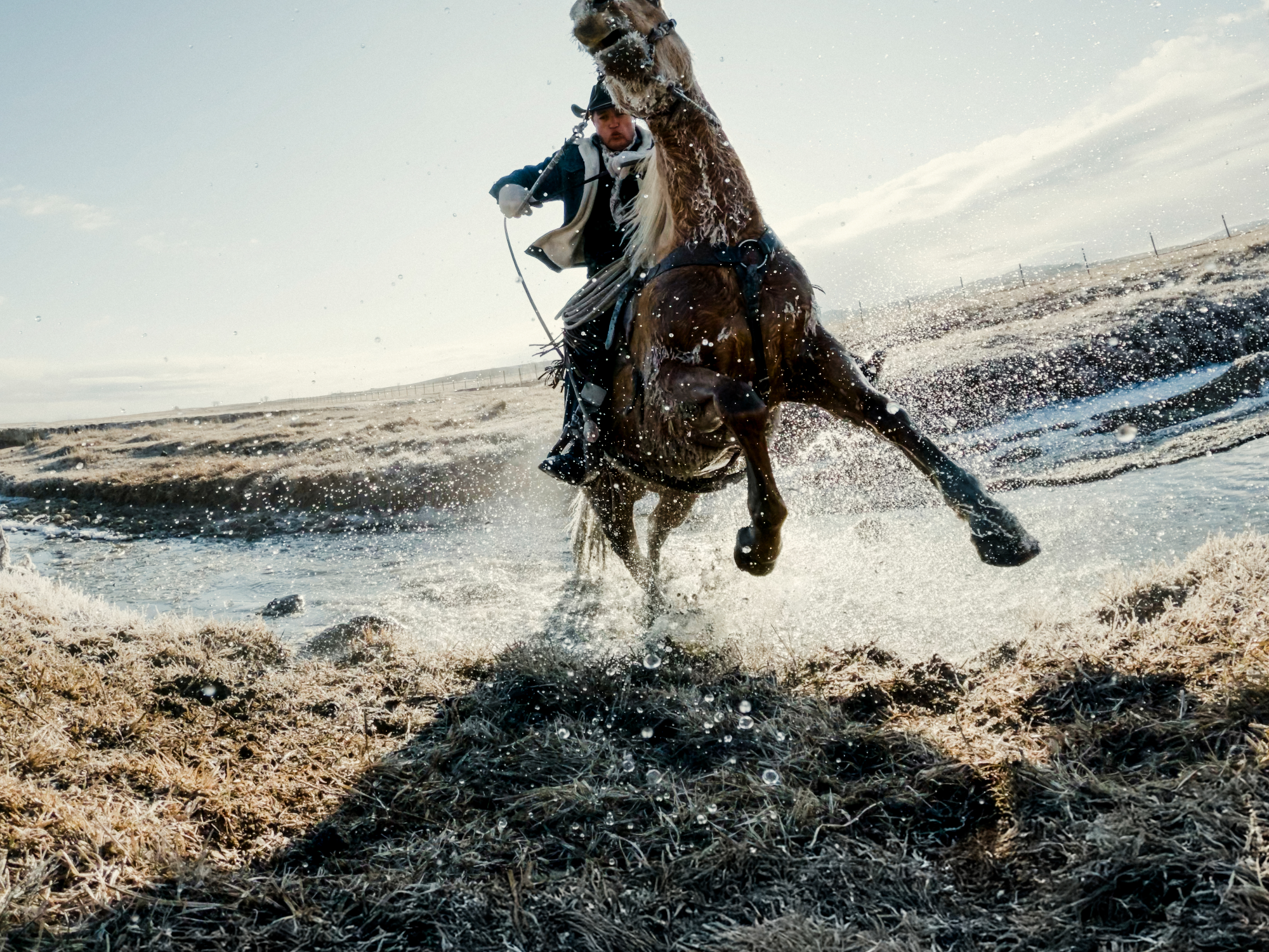 Ein Reiter auf einem braunen Pferd springt durch eine Wasserstelle im Freien.