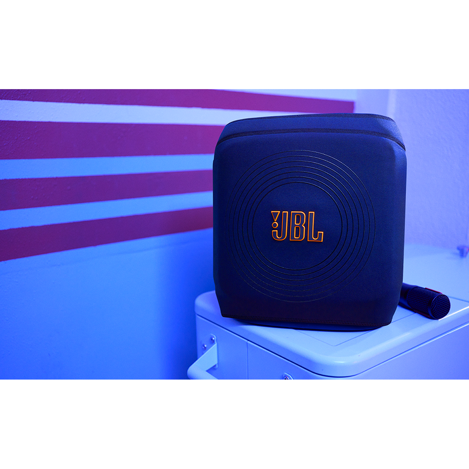 Een blauwe JBL luidspreker met oranje logo en microfoon op een witte kast.