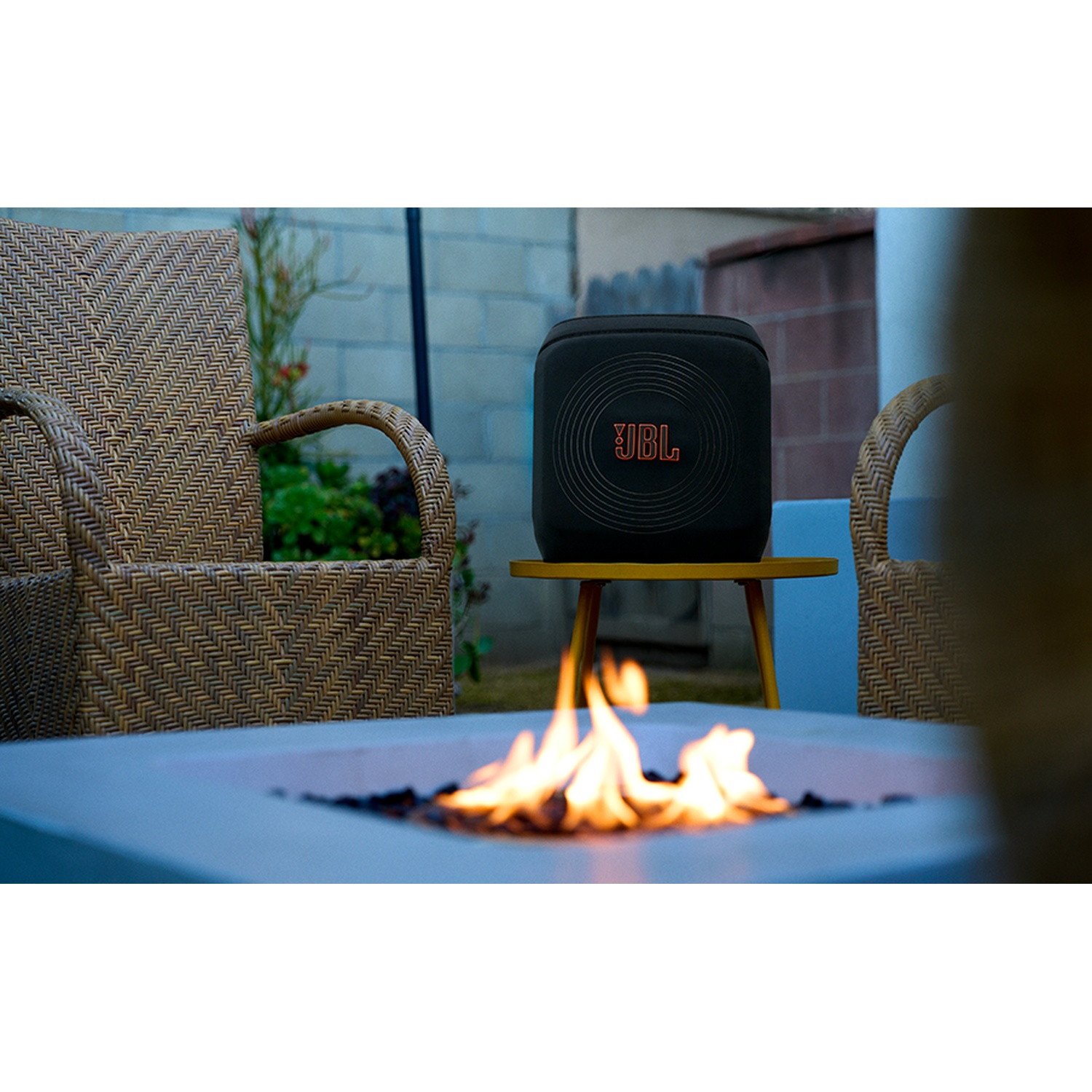 Een zwarte JBL speaker staat op een gele tafel naast een vuurkorf met vlammen.