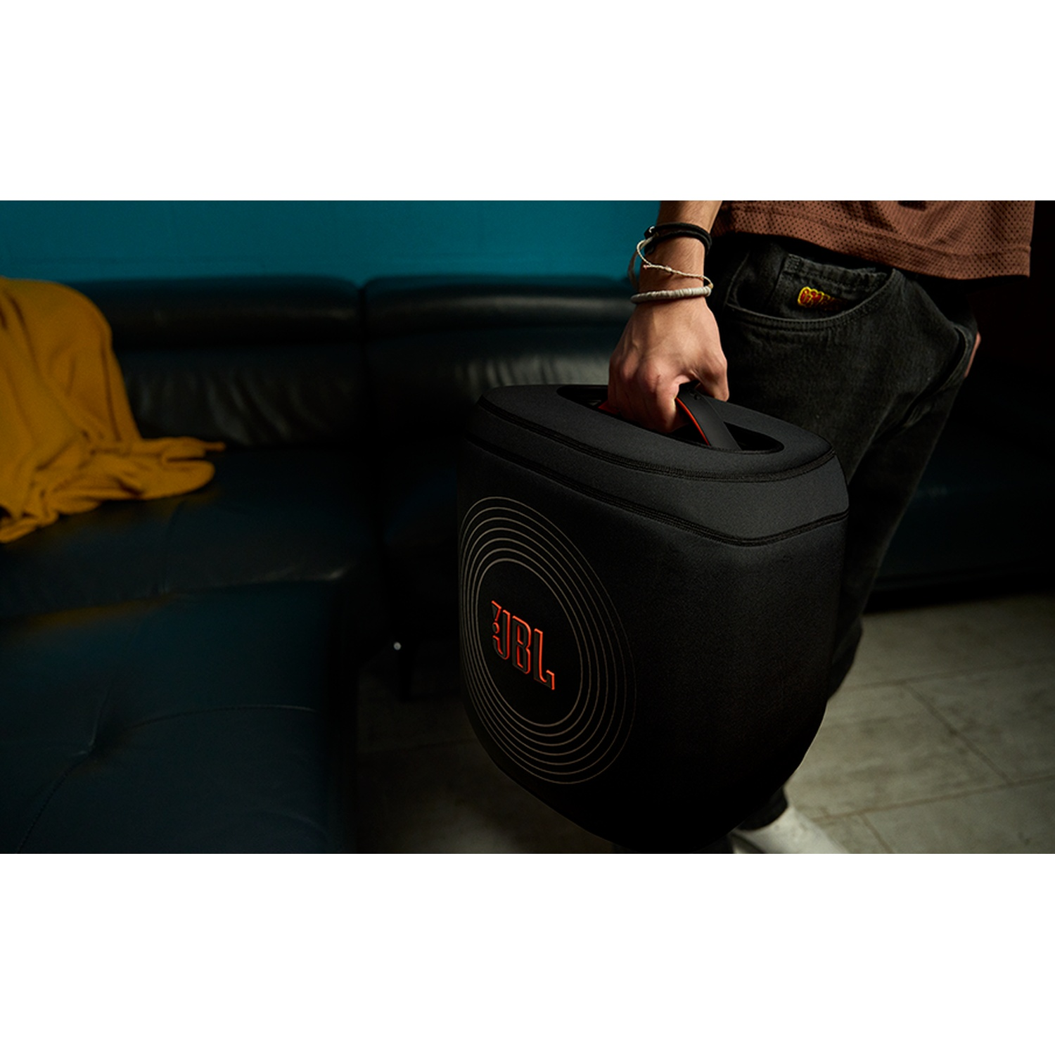 Persoon draagt zwarte JBL tas met oranje logo over een bank.