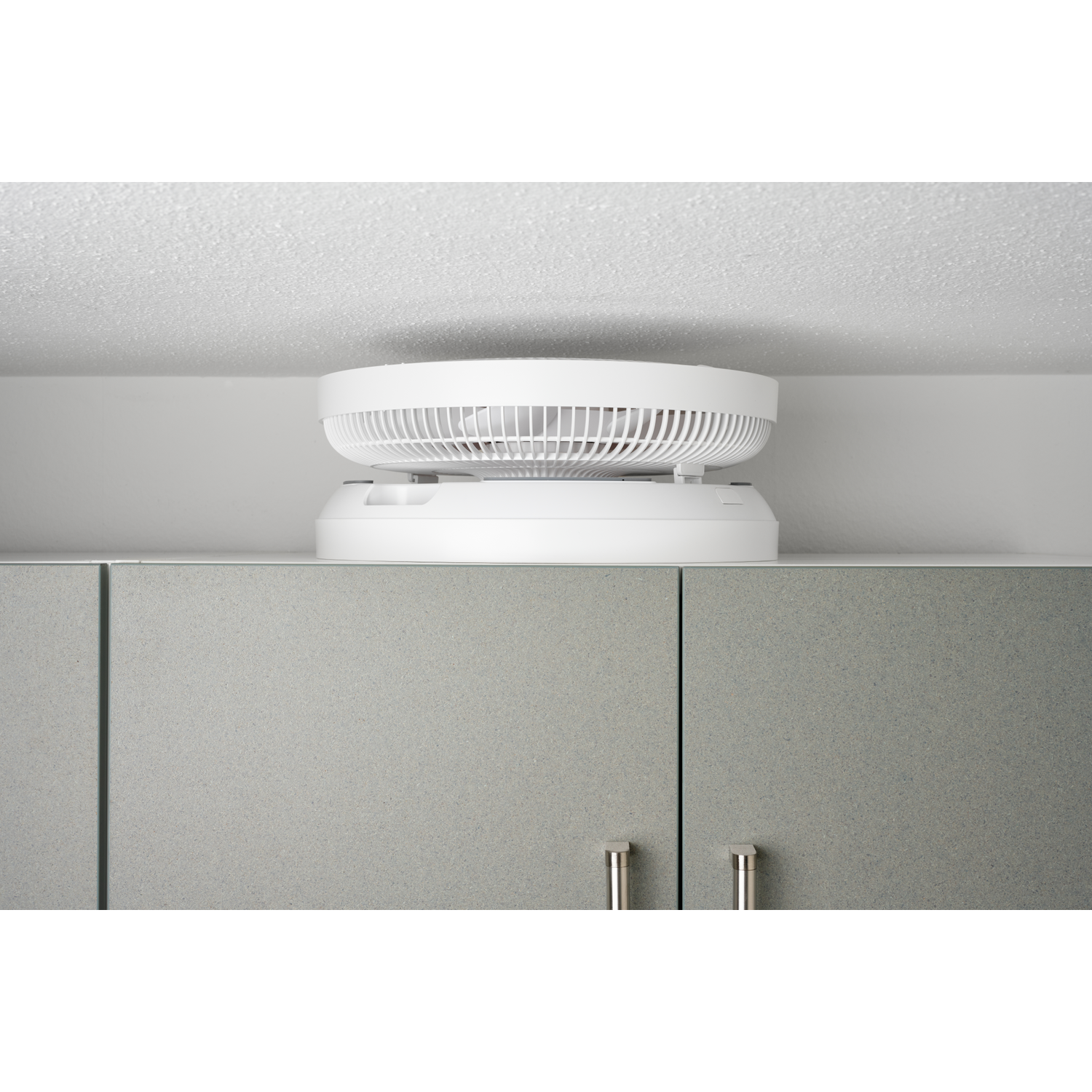 A white fan sits on top of a gray cabinet beneath a ceiling.