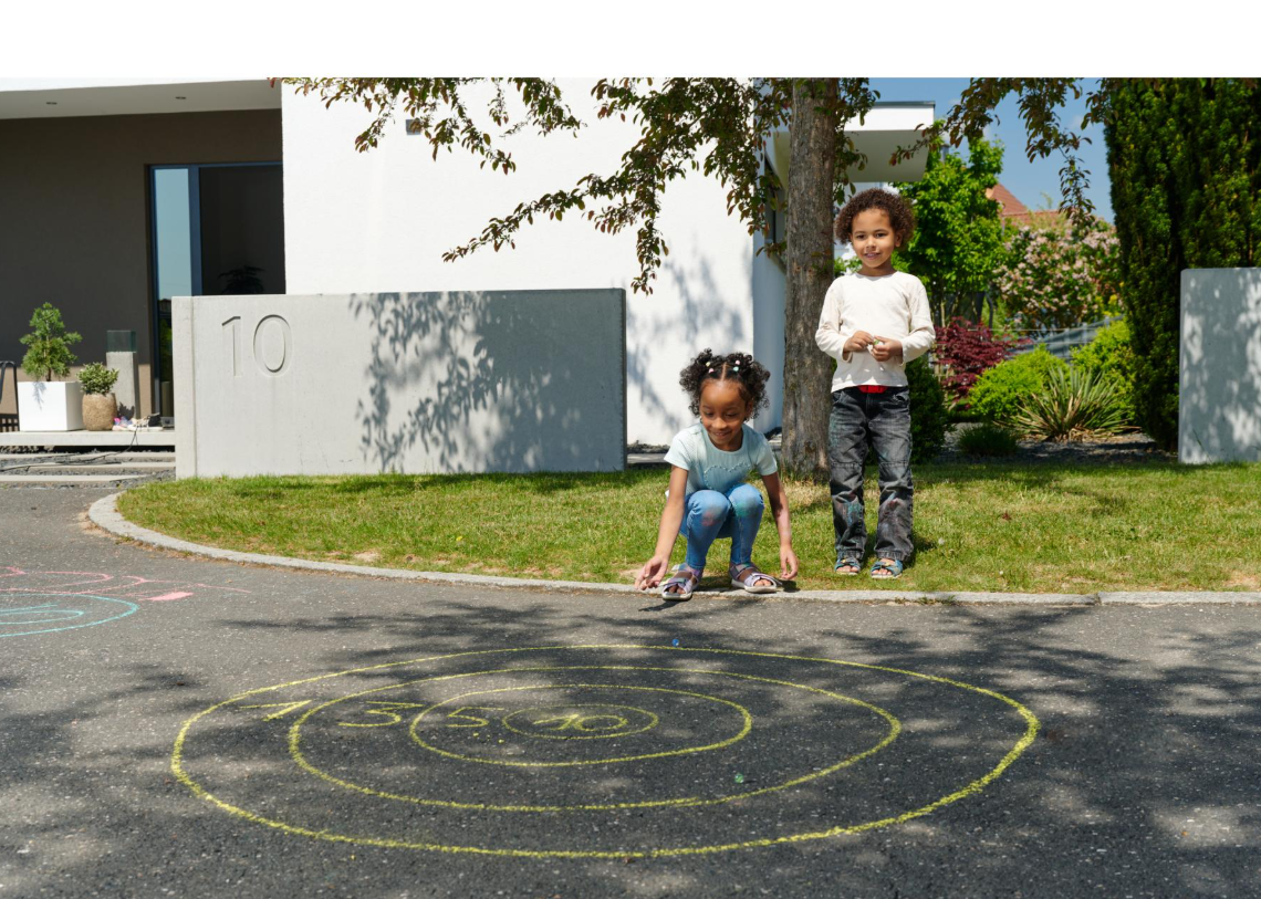 Zwei Kinder spielen mit Murmeln auf einem Kreisspiel mit Zahlen, das mit Kreide auf Asphalt gemalt wurde.