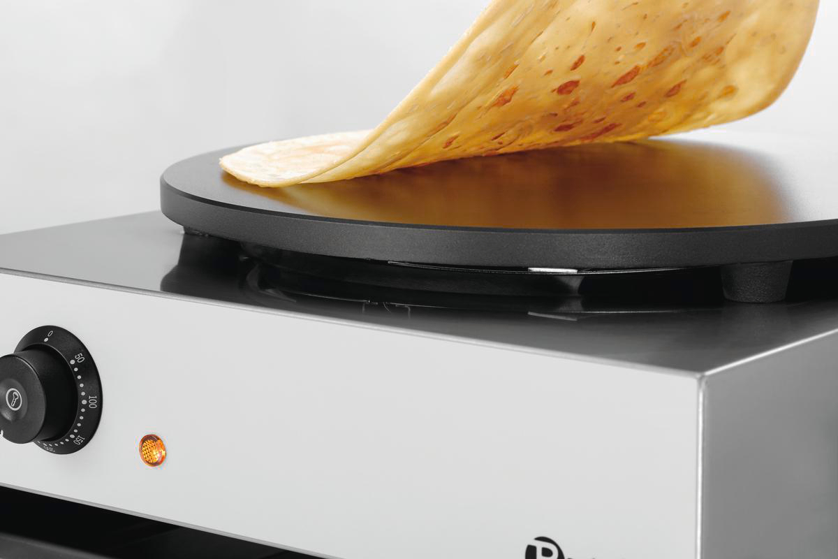 Ein Crêpe wird von einem Crêpes-Maker gehoben. Die Platte ist schwarz, der Crêpe goldbraun.