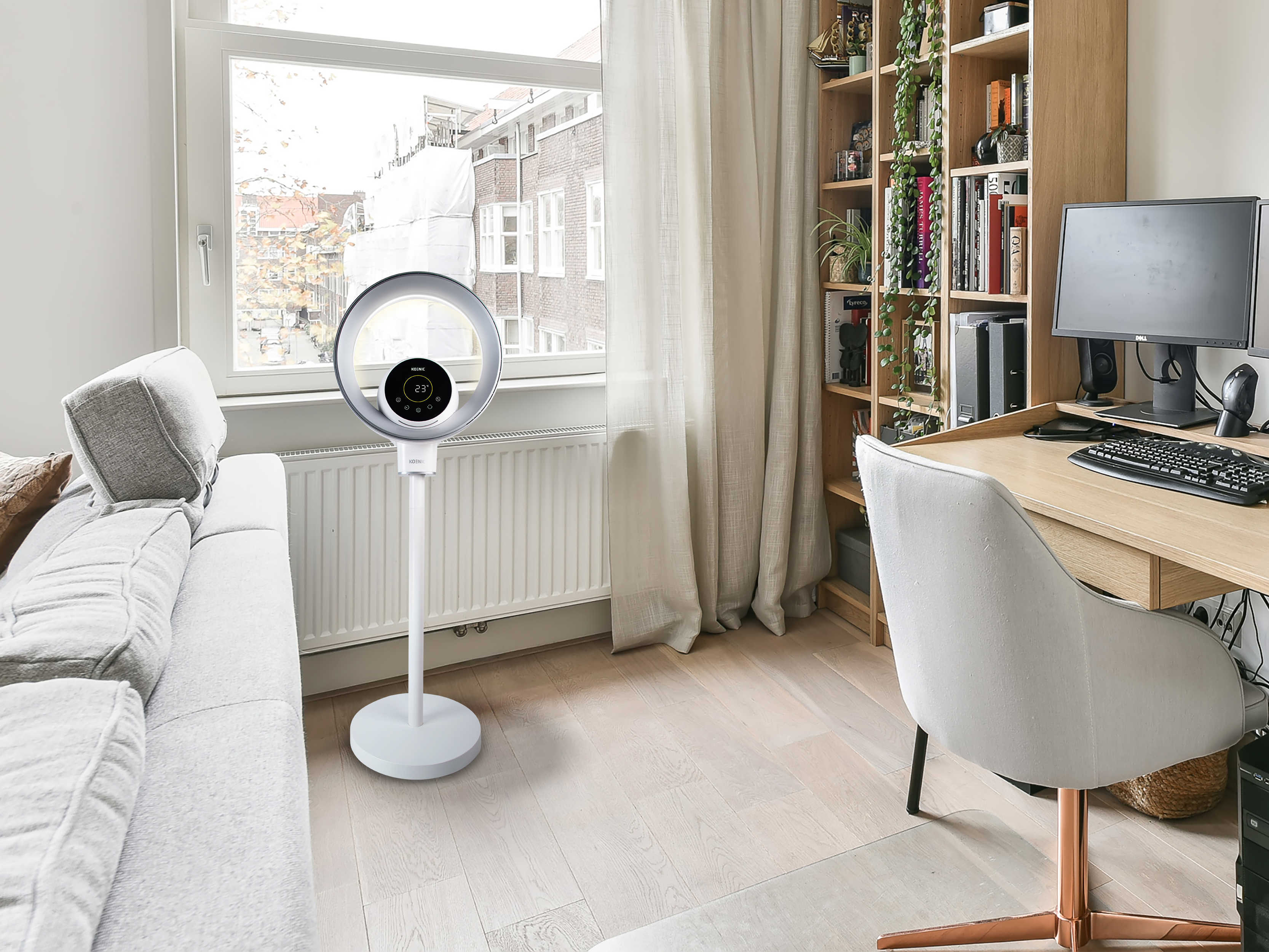 Ein helles Wohnzimmer mit Sofa, Schreibtisch, Computer und einem Standventilator.