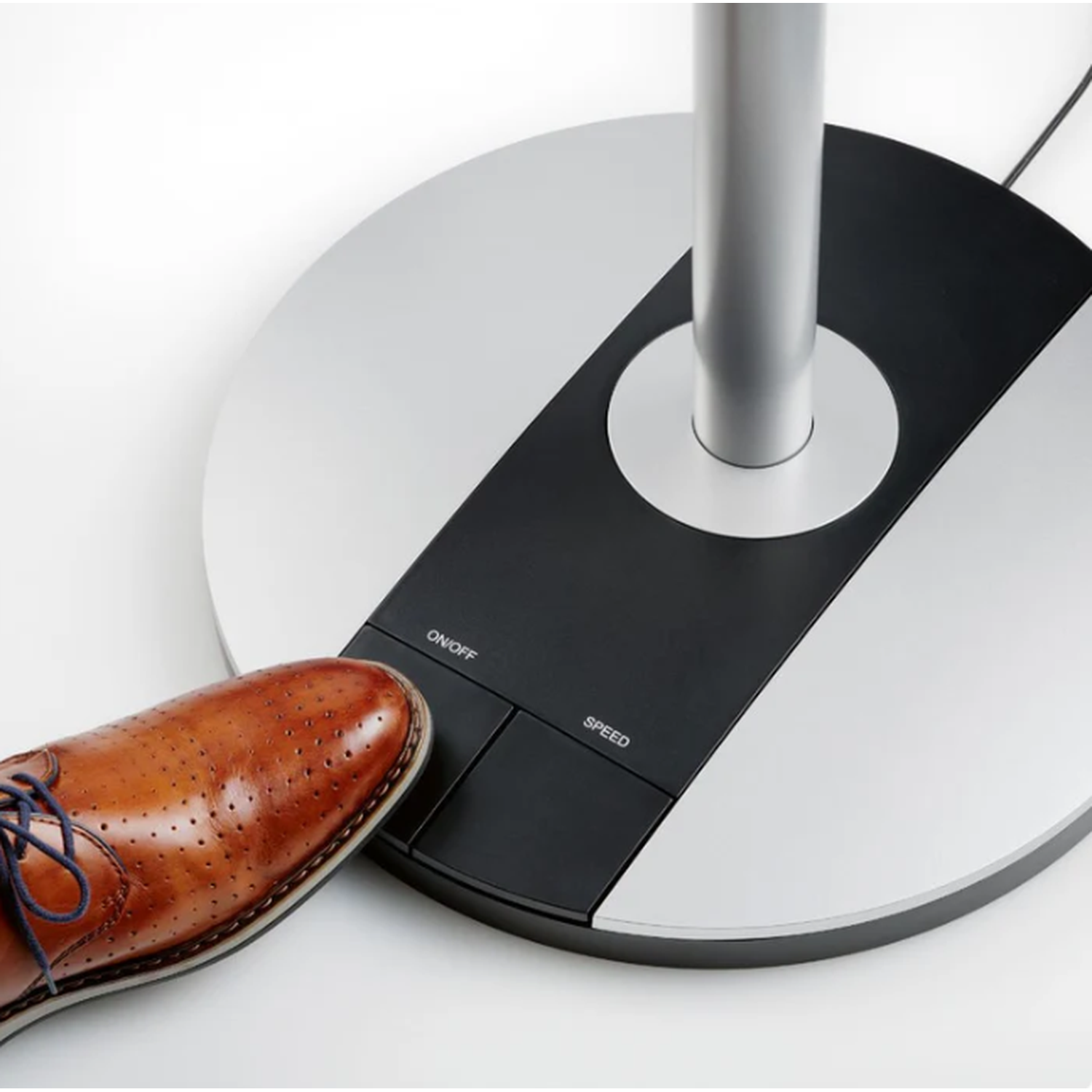 A brown leather shoe with blue laces presses the ON/OFF button on a sleek fan base.