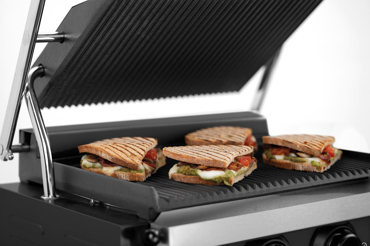 Vier gegrillte Sandwiches auf einer Grillplatte, mit sichtbarer Füllung.