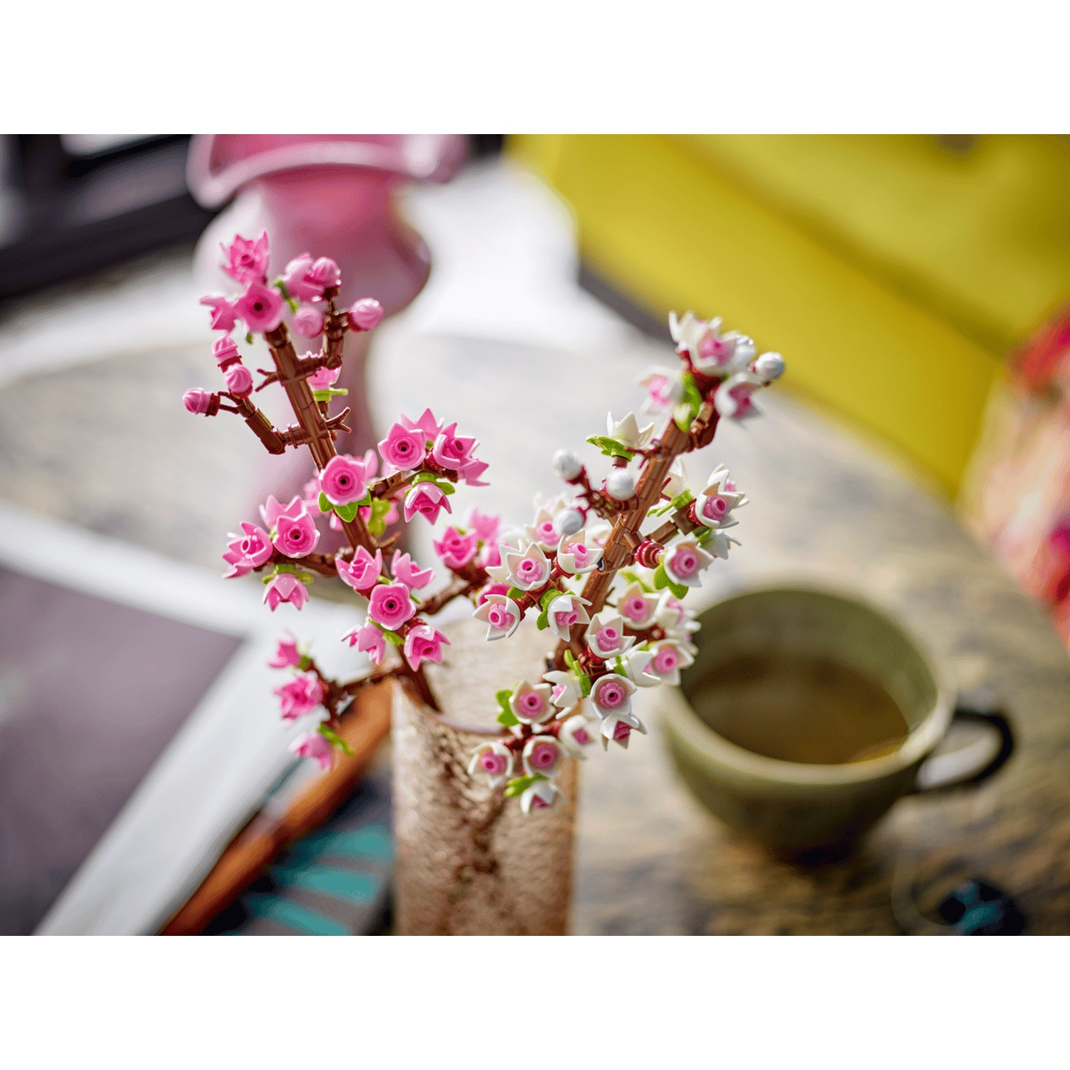 Tak met roze en witte bloemen in een vaas naast een kopje.