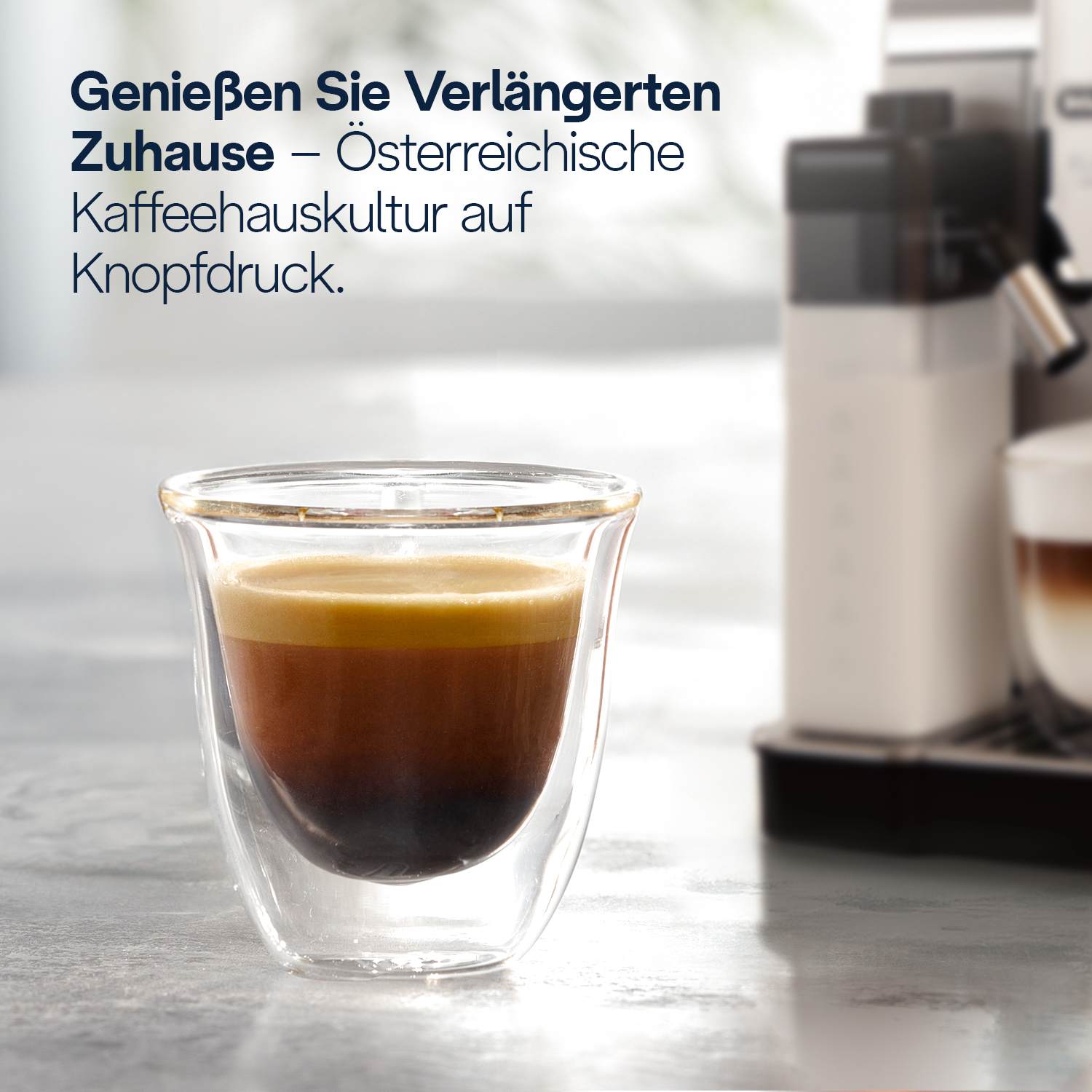 Ein Glas Espresso mit Crema steht auf einem Tisch neben einer Kaffeemaschine.