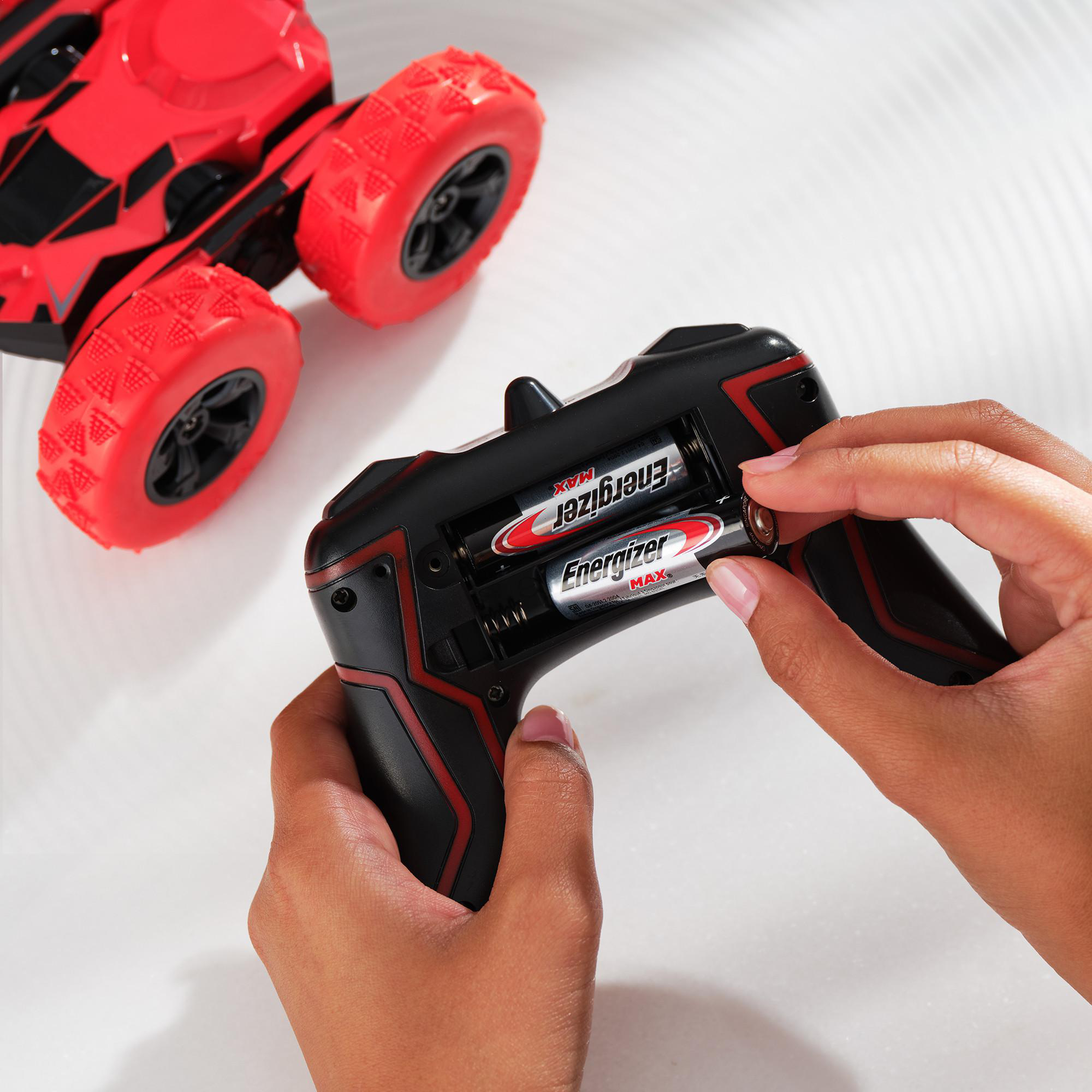 Hände setzen Batterien in eine schwarze Fernbedienung neben einem roten Spielzeugauto ein.