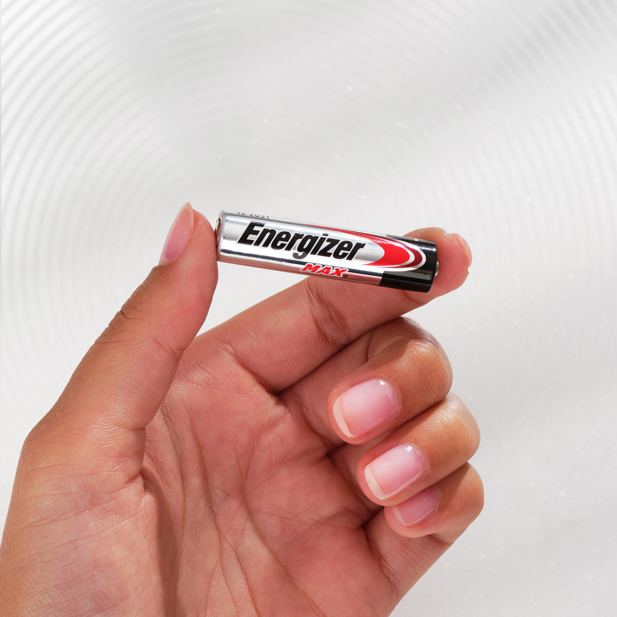 Eine Hand hält eine silberne Energizer Max AA-Batterie vor einem strukturierten Hintergrund.