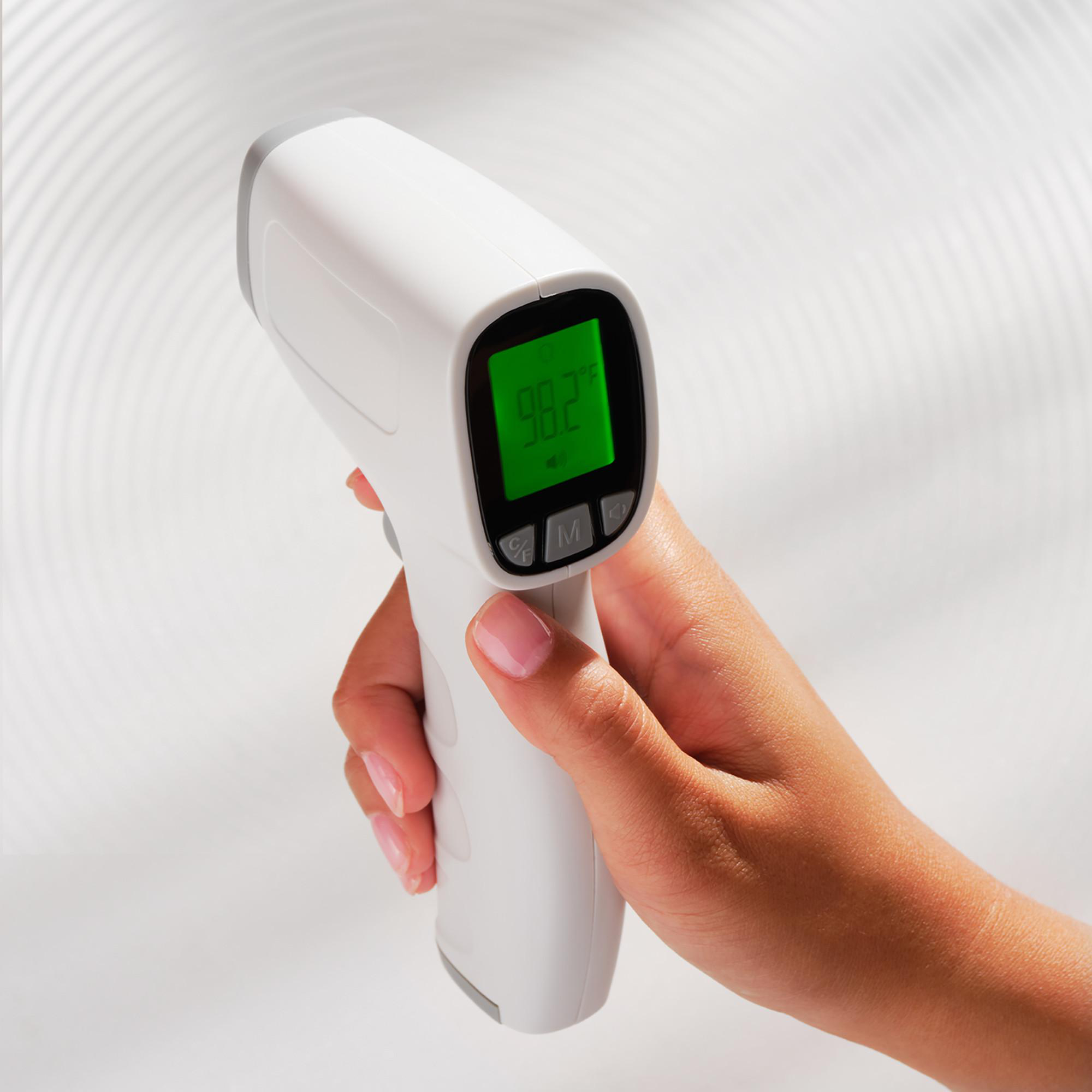 Eine Hand hält ein weißes Digitalthermometer mit 98,2 F auf grünem Bildschirm.