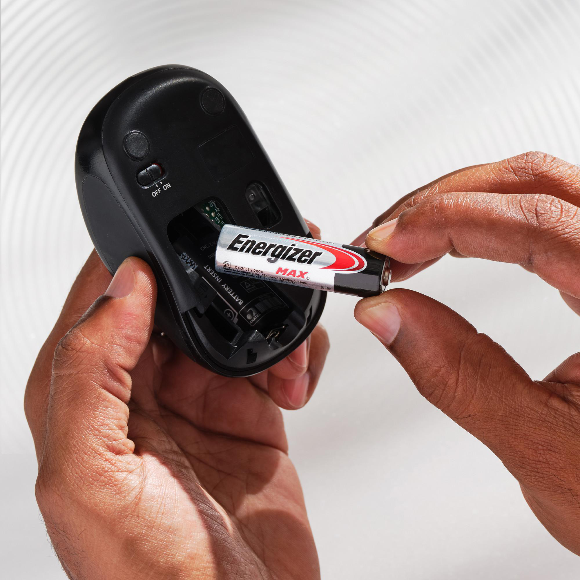 Hände setzen eine Energizer MAX Batterie in eine schwarze Computermaus ein.
