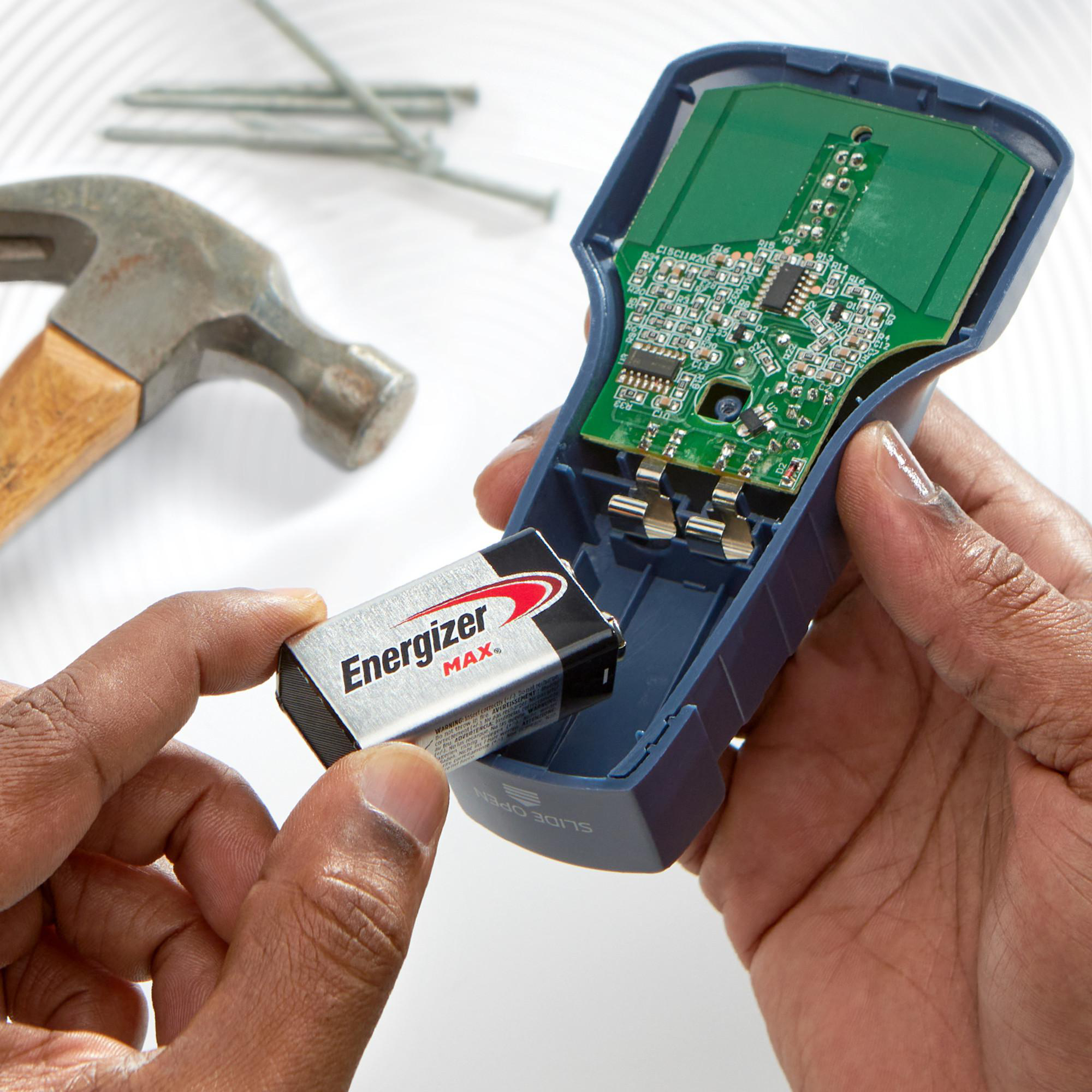 Hände setzen eine 9V-Batterie in ein blaues Gehäuse mit Leiterplatte ein.