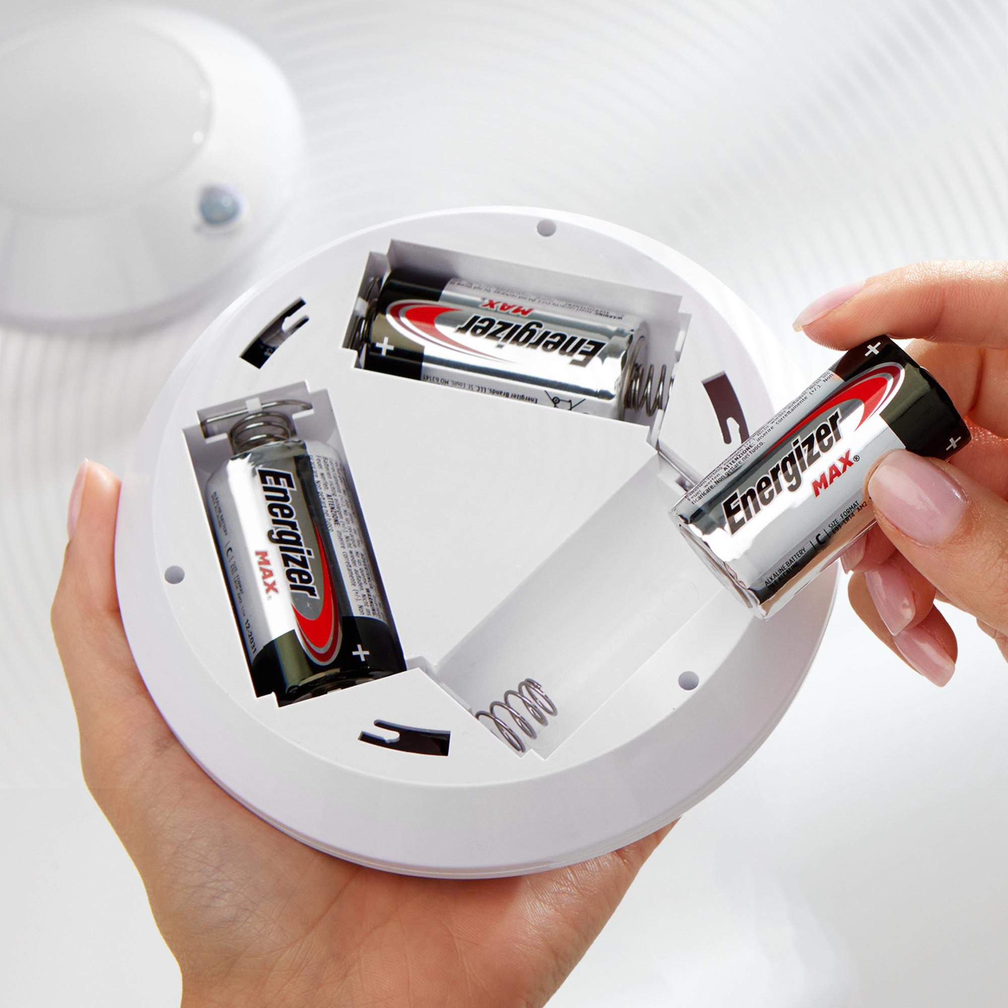 Hände legen Energizer MAX Batterien in ein weißes Gerät ein.
