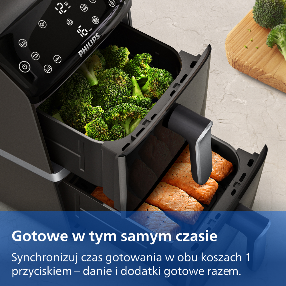 Czarna frytkownica beztłuszczowa z dwoma szufladami, wypełniona brokułami i filetami łososia.
